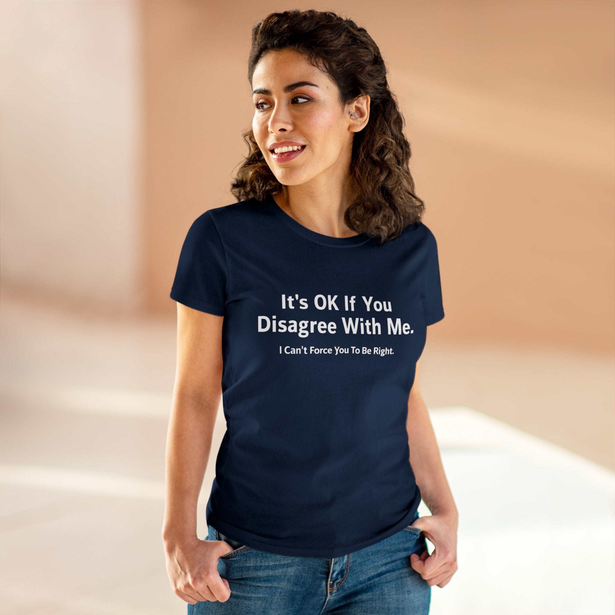 A woman wearing a navy blue "It's Ok If You Disagree With Me - Women's Tee" stands in a softly lit room. The pre-shrunk fabric ensures her comfort while making a bold statement.
