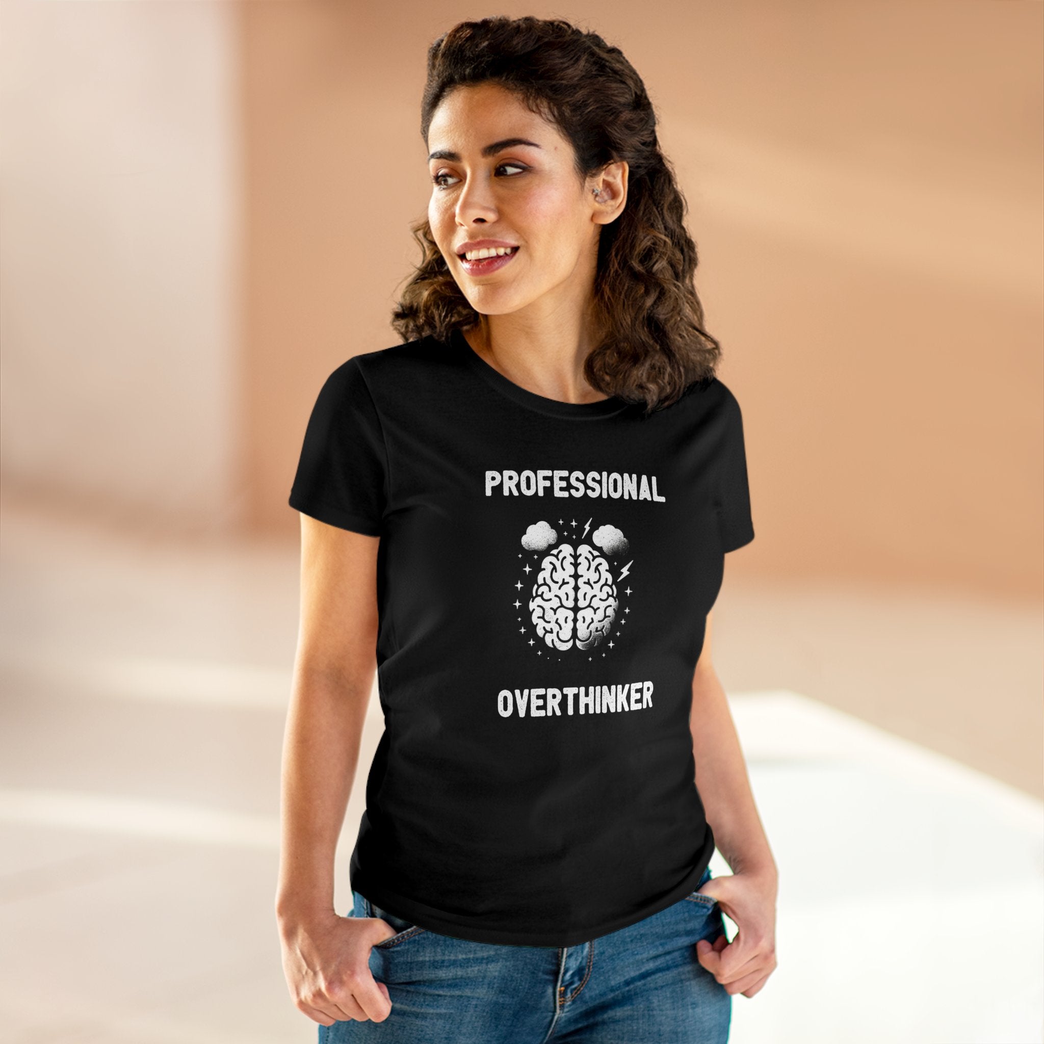 A woman wearing a black Professional Overthinker - Women's Tee with the text "Professional Overthinker" and an image of a brain printed on it, standing indoors and smiling. The semi-fitted, pre-shrunk comfort adds to her confident demeanor.