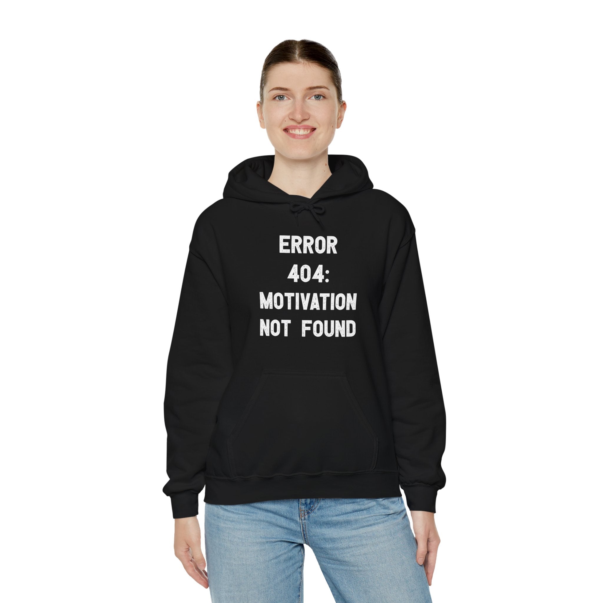 A person wearing an Error 404: Motivation not found - Hooded Sweatshirt stands against a white background, smiling with hands in pockets.