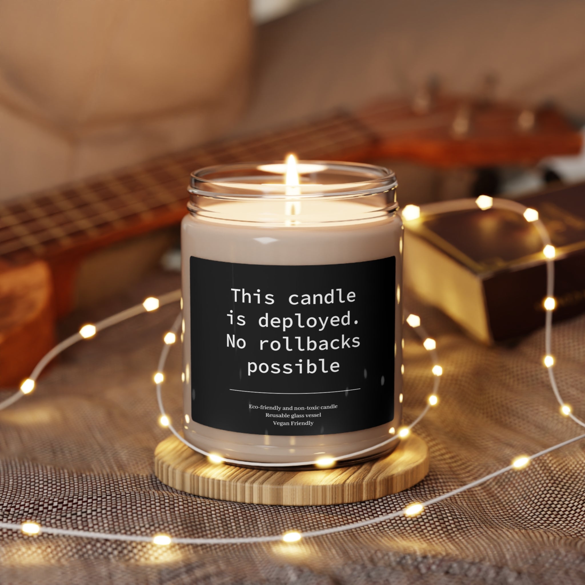 A lit This Candle Deployed - No Rollbacks- Scented Soy Candle with a humorous label surrounded by fairy lights.