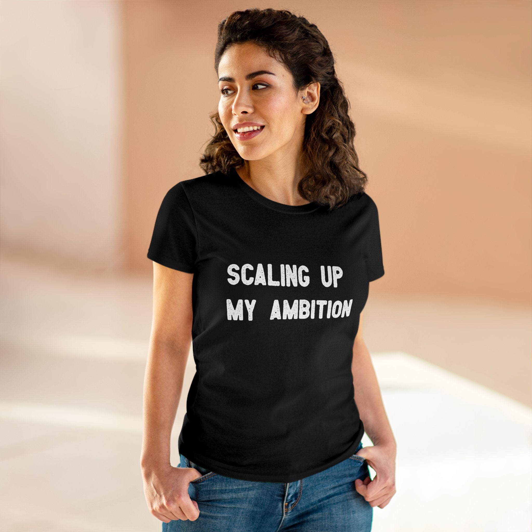 A woman stands smiling in the "Scaling Up My Ambition" women's tee, made from pre-shrunk cotton and featuring bold text.