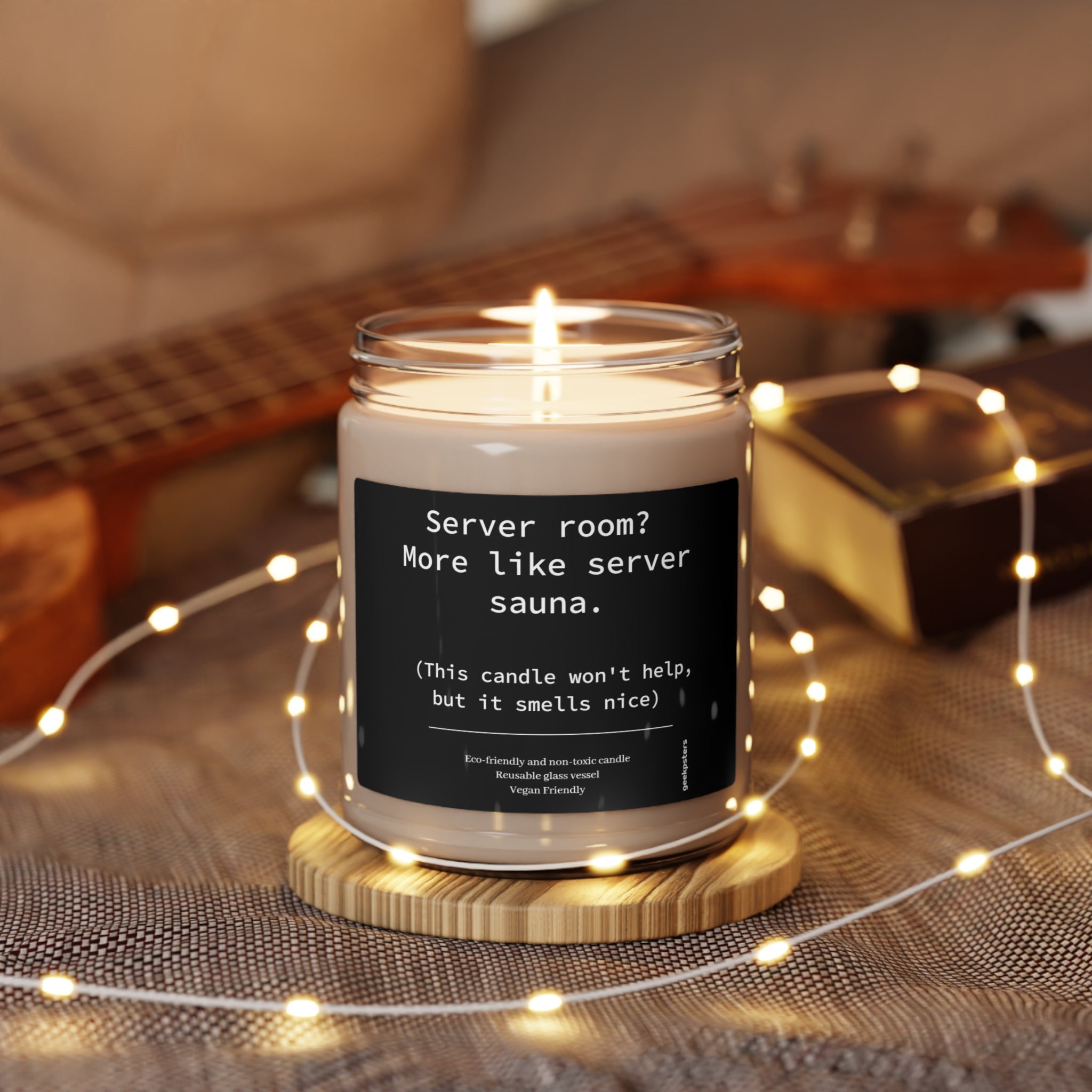 A lit Server Room? More Like Server Sauna scented candle with a humorous label on a wooden holder amidst fairy lights, featuring a natural soy wax blend.