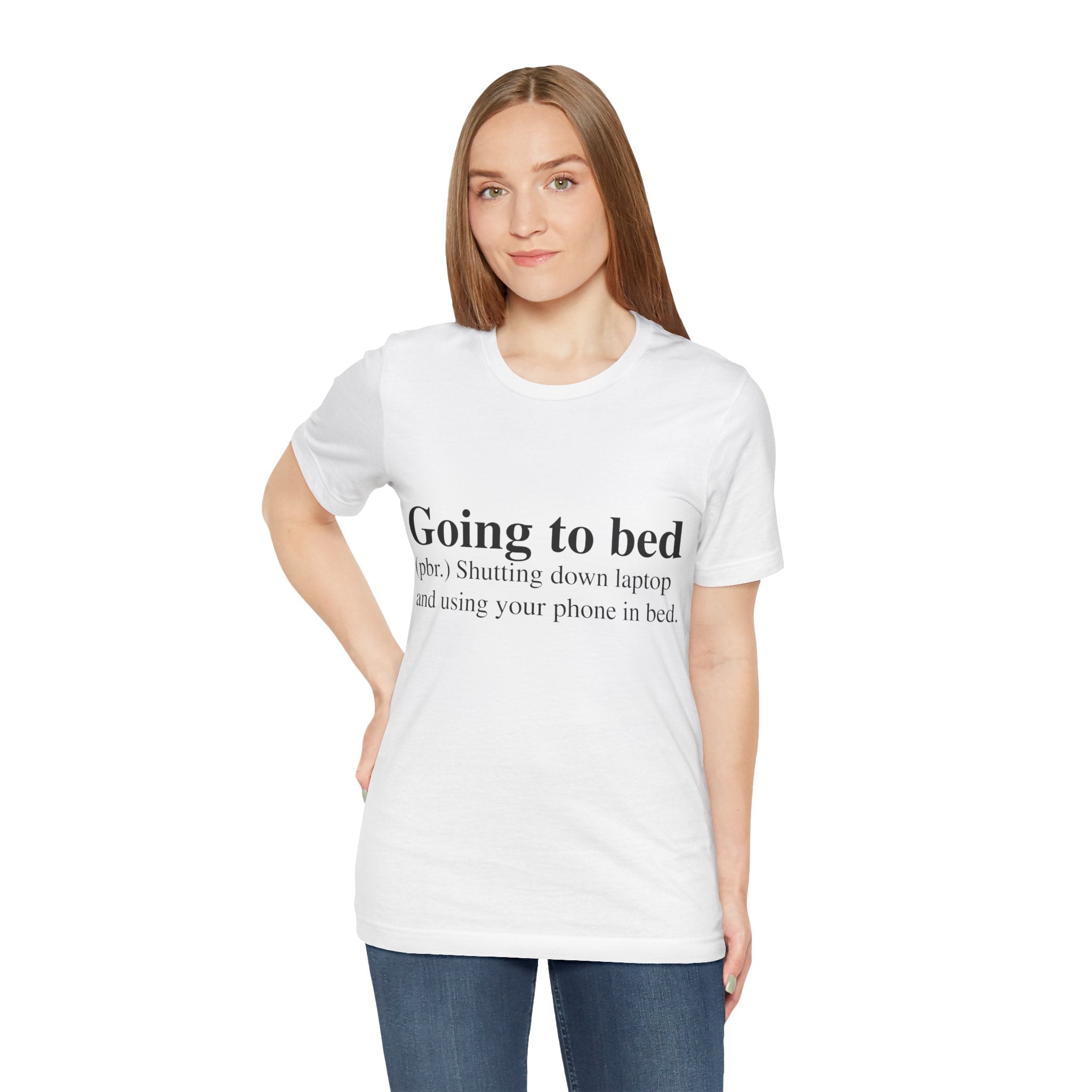 Woman in a white, short sleeve Going to Bed T-shirt standing against a plain background.