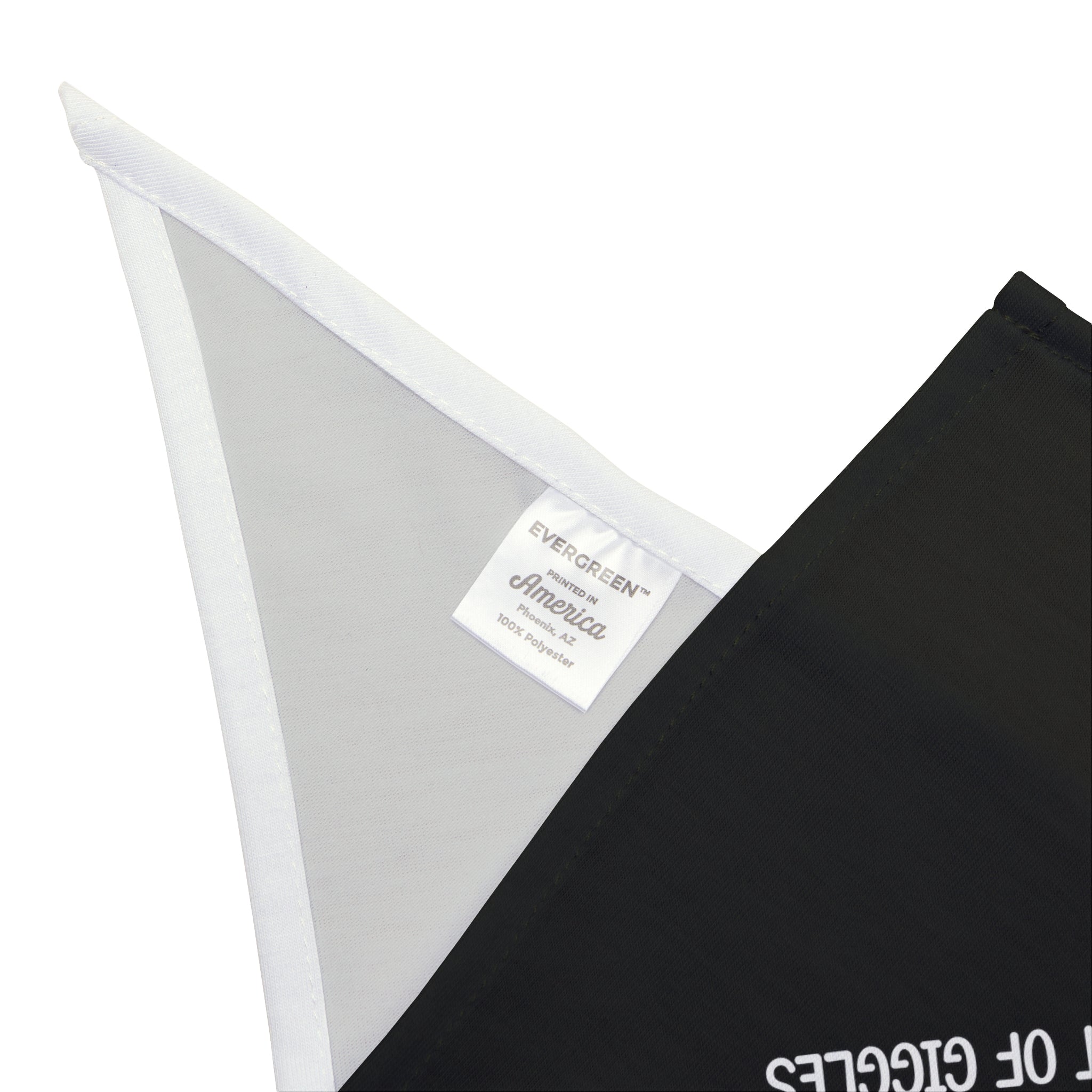 Close-up image of a corner of a black fabric with a white tag that reads "EVERGREEN America 100% polyester," showcasing its classy and durable, soft-spun polyester perfect for a stylish He-He - Pet Bandana.