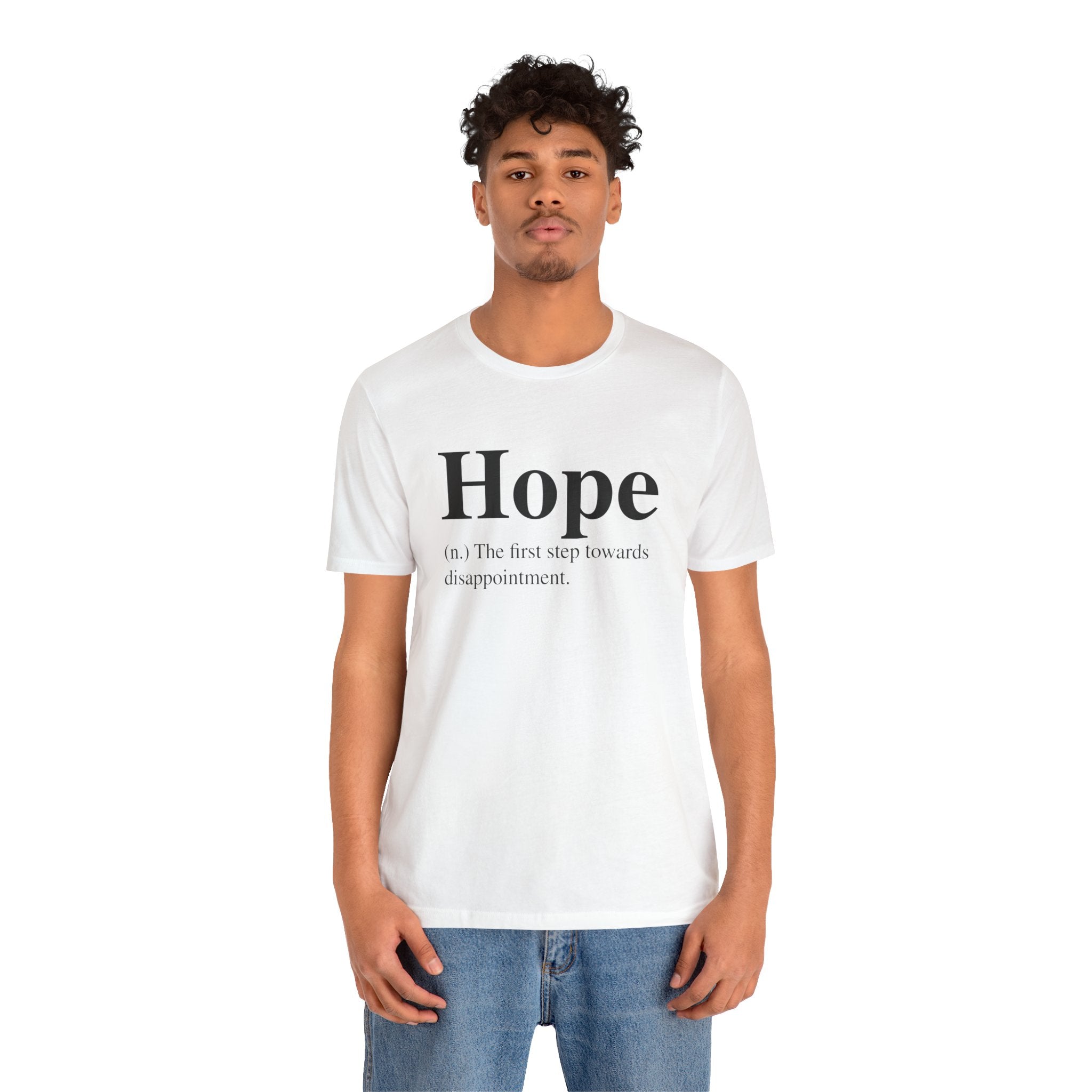 A young man wearing a soft cotton, white unisex Hope T-Shirt with the word "hope" and its cynical definition printed on it, paired with blue jeans.