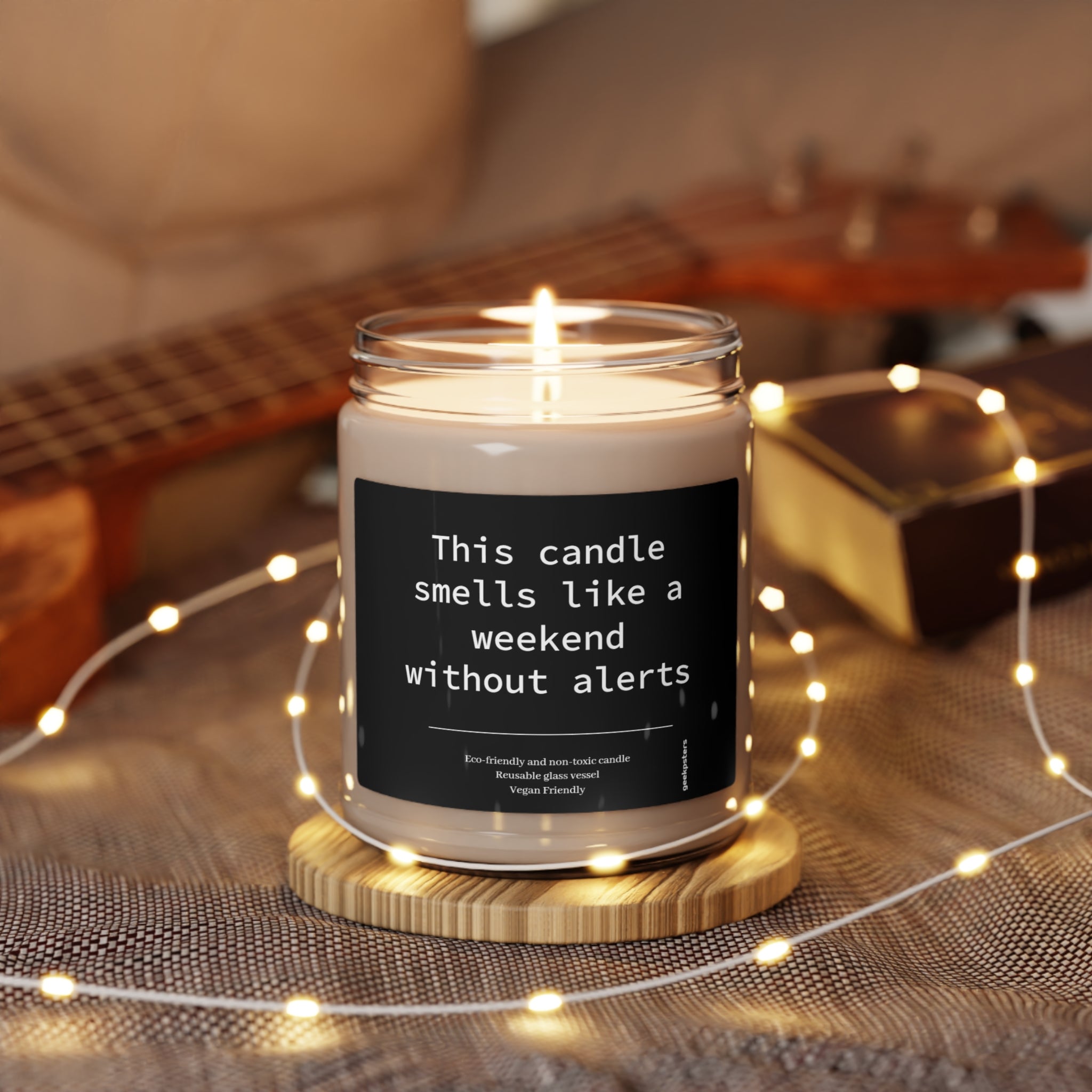 A "This Candle Smells Like a Weekend Without Alerts - Scented Soy Candle, 9oz" with humorous labeling is lit amidst a cozy setting with warm lights and wooden accents.