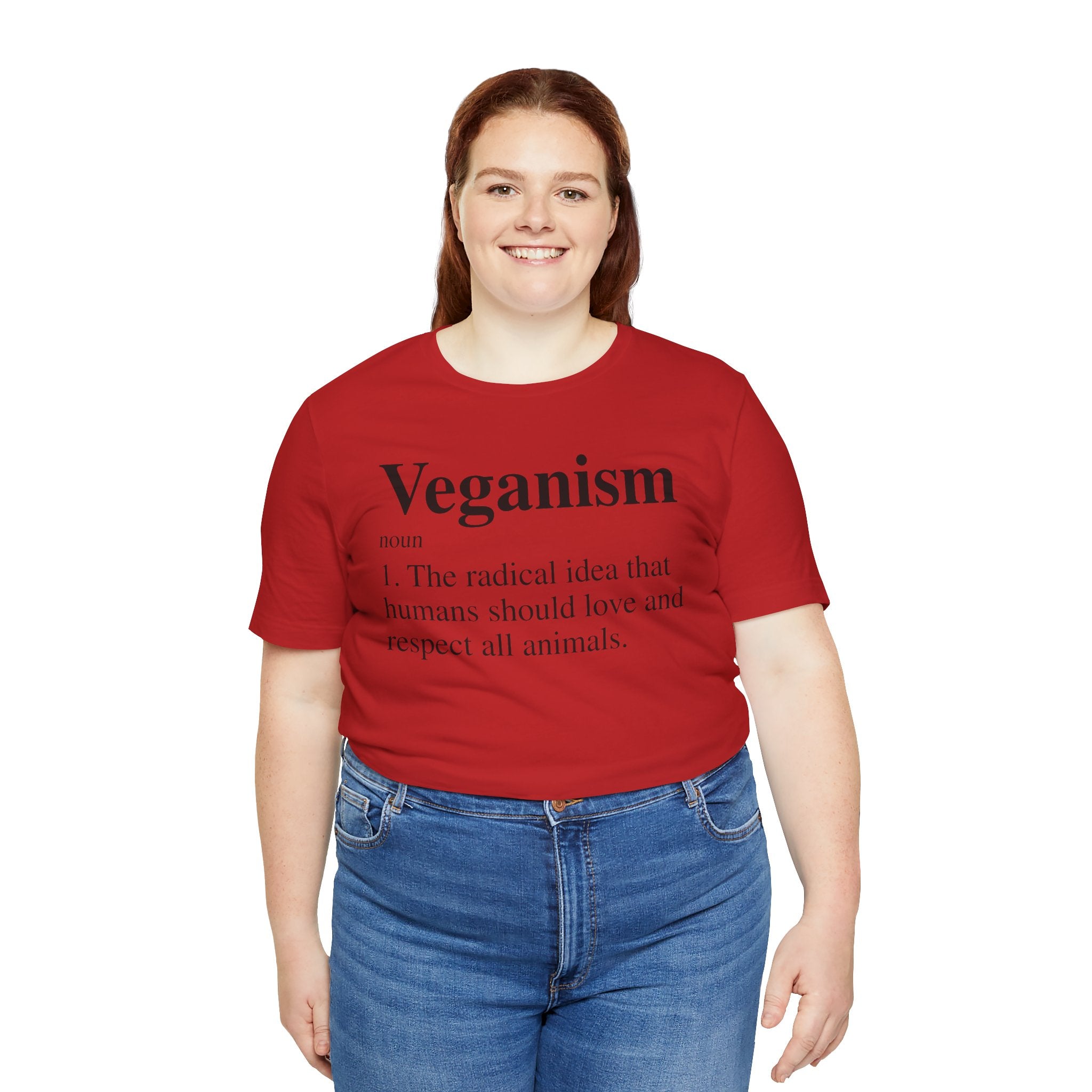 A woman in a red Veganism T-Shirt stands smiling, wearing blue jeans on a white background.