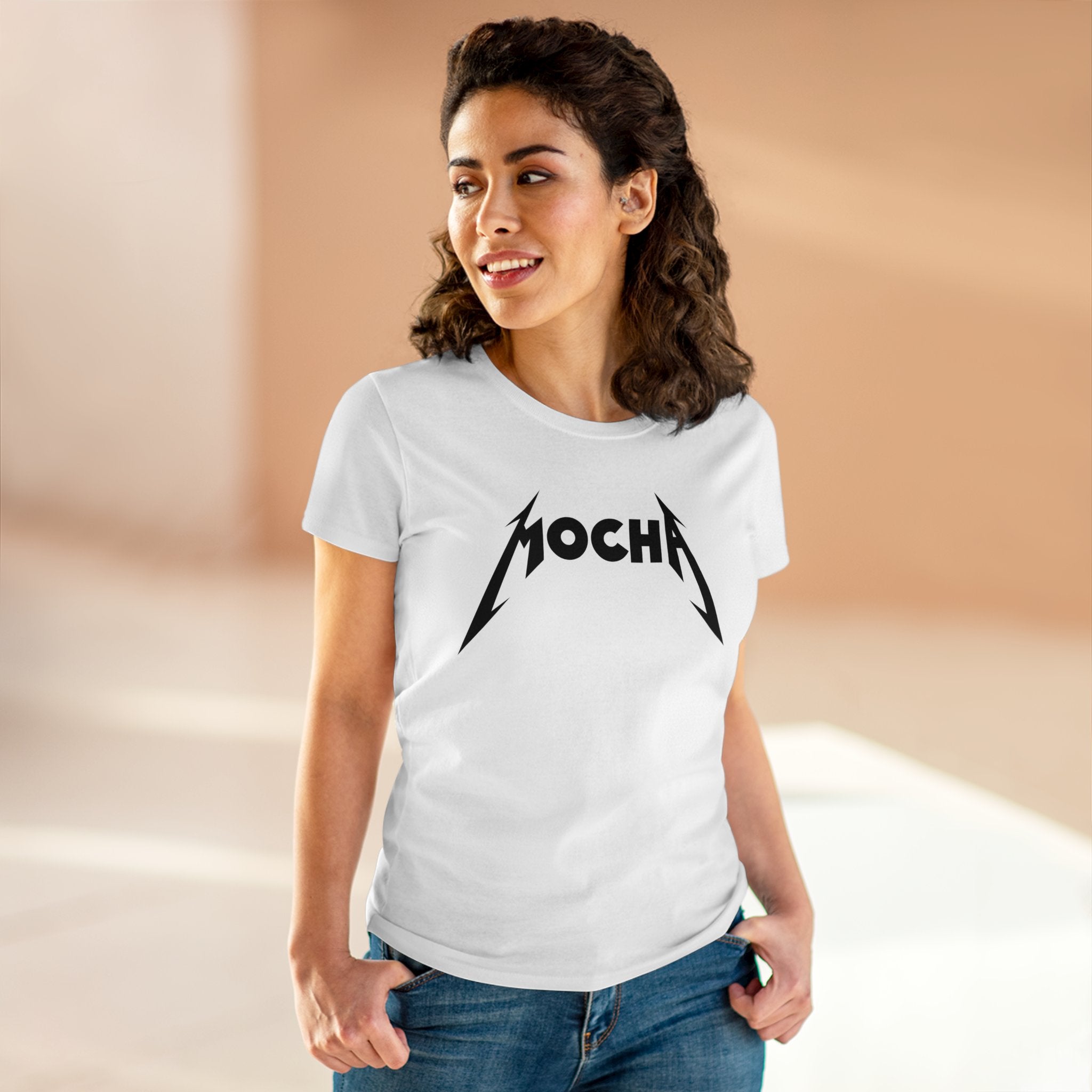 A person with curly hair is wearing a sleek white t-shirt with the word "Mocha - Women's Tee" written in a stylized, bold font. The shirt, made of soft light cotton and featuring a pre-shrunk fit, gleams under the well-lit room's illumination.