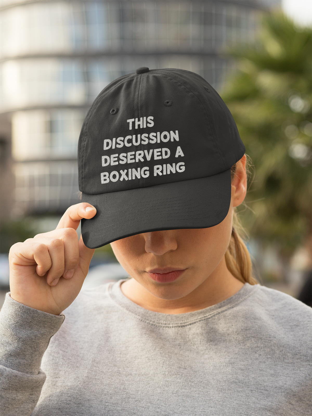 'This Discussion Deserved a Boxing Ring' dad hat in black, woman wearing it outdoors, funny sarcastic gift