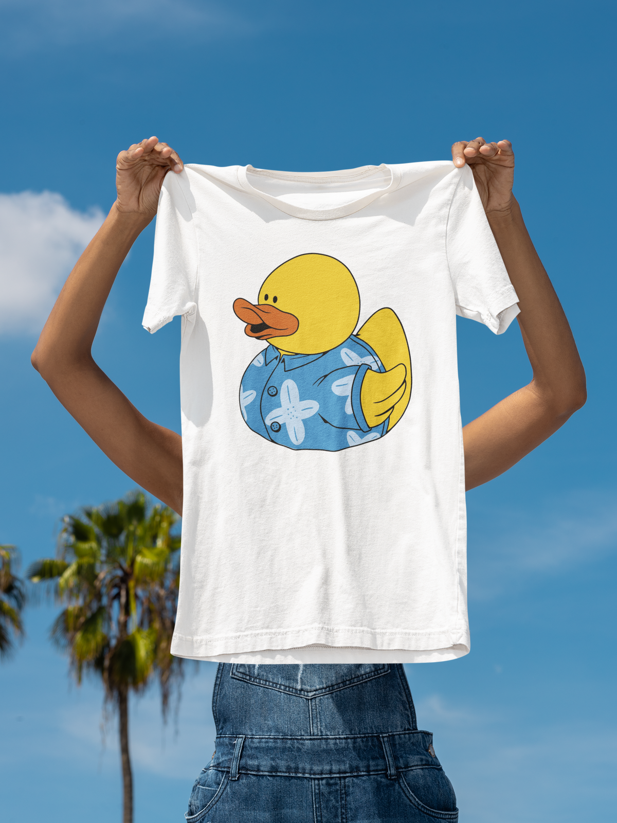 Hawaii duck t-shirt in white, held up outdoors against a palm tree sky backdrop, funny summer gift