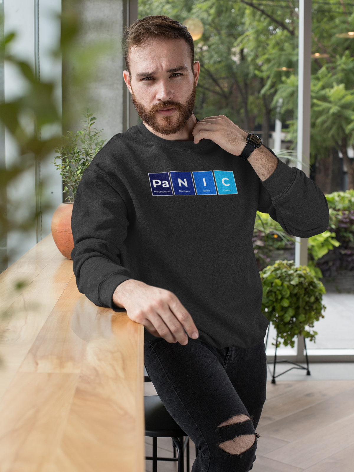 'Pa-N-I-C' periodic table sweatshirt in black, man leaning on a railing outdoors, casual style photo