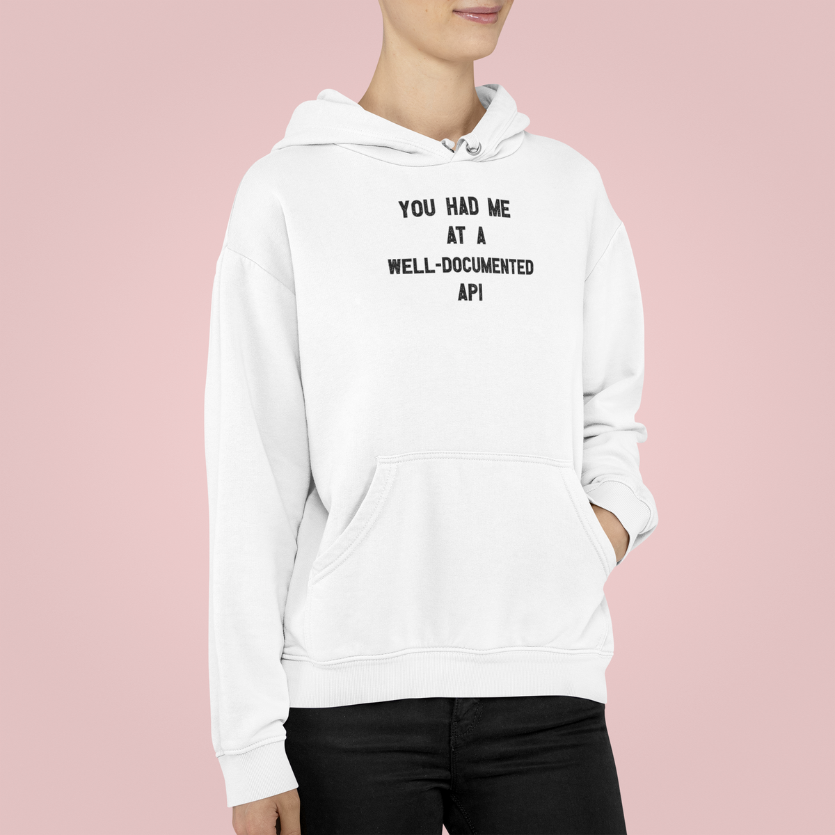 'You Had Me At a Well-Documented API' hoodie in white, woman wearing it, pink backdrop, coder gift