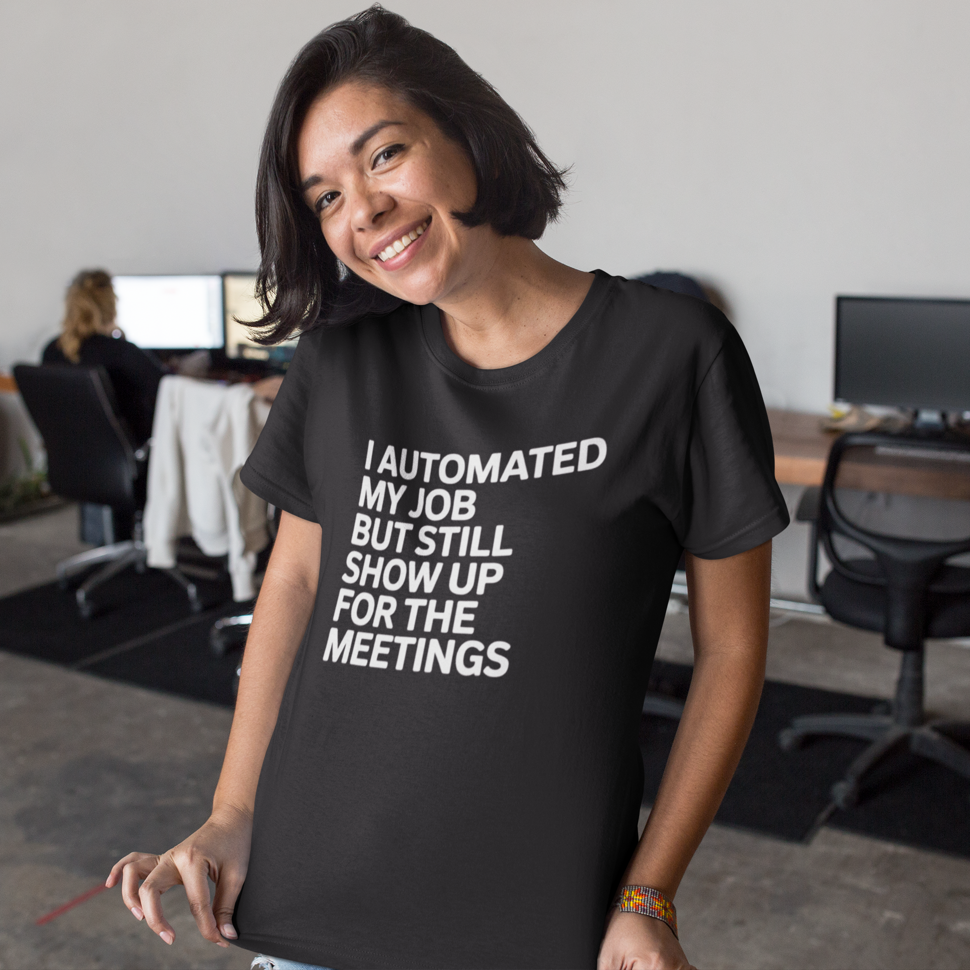 A woman smiles at the camera in an office while wearing the "I Automated My Job But Still Show Up for the Meetings" shirt.