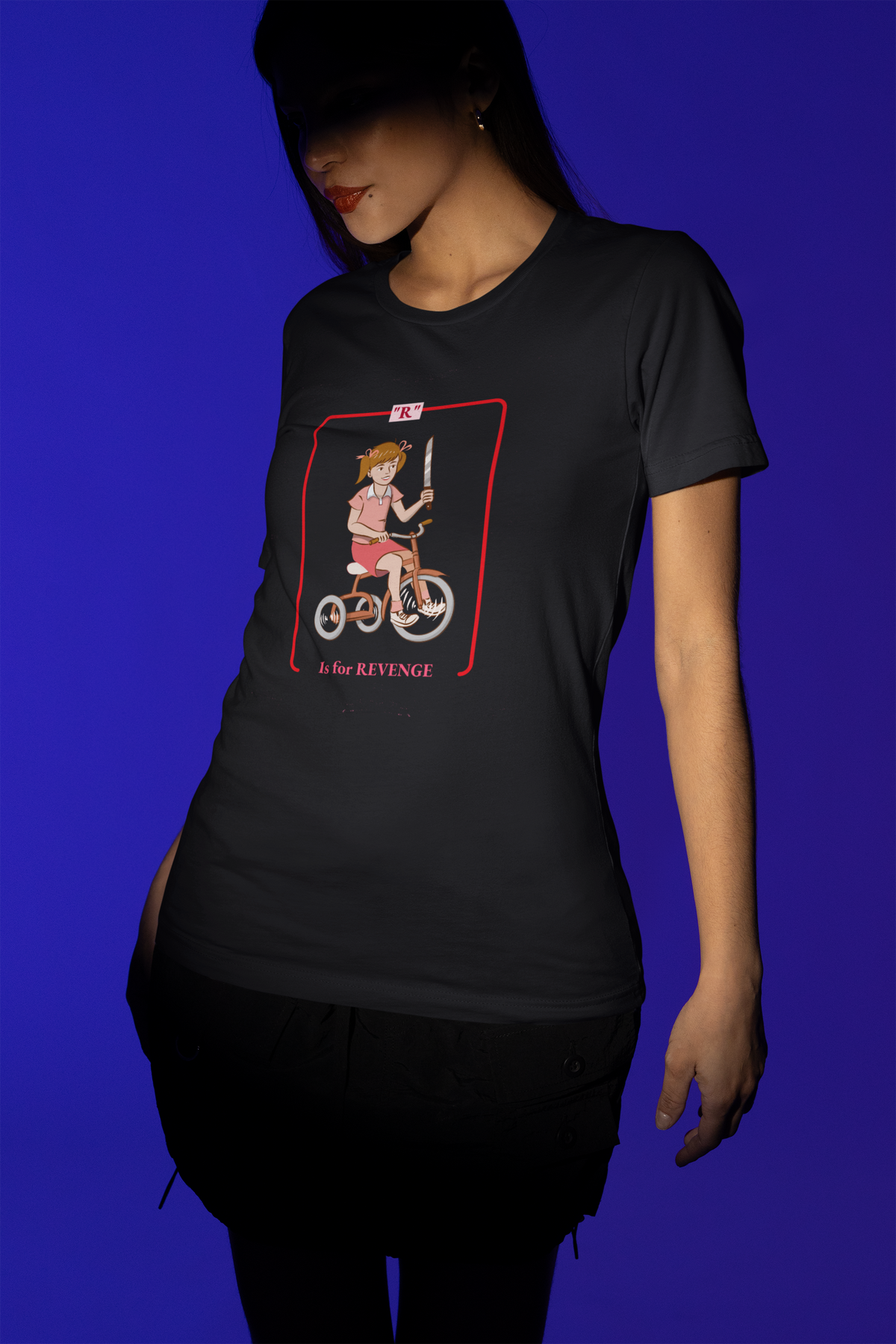 'R is for Revenge' tricycle girl graphic t-shirt in black, woman wearing it on blue backdrop, funny gift