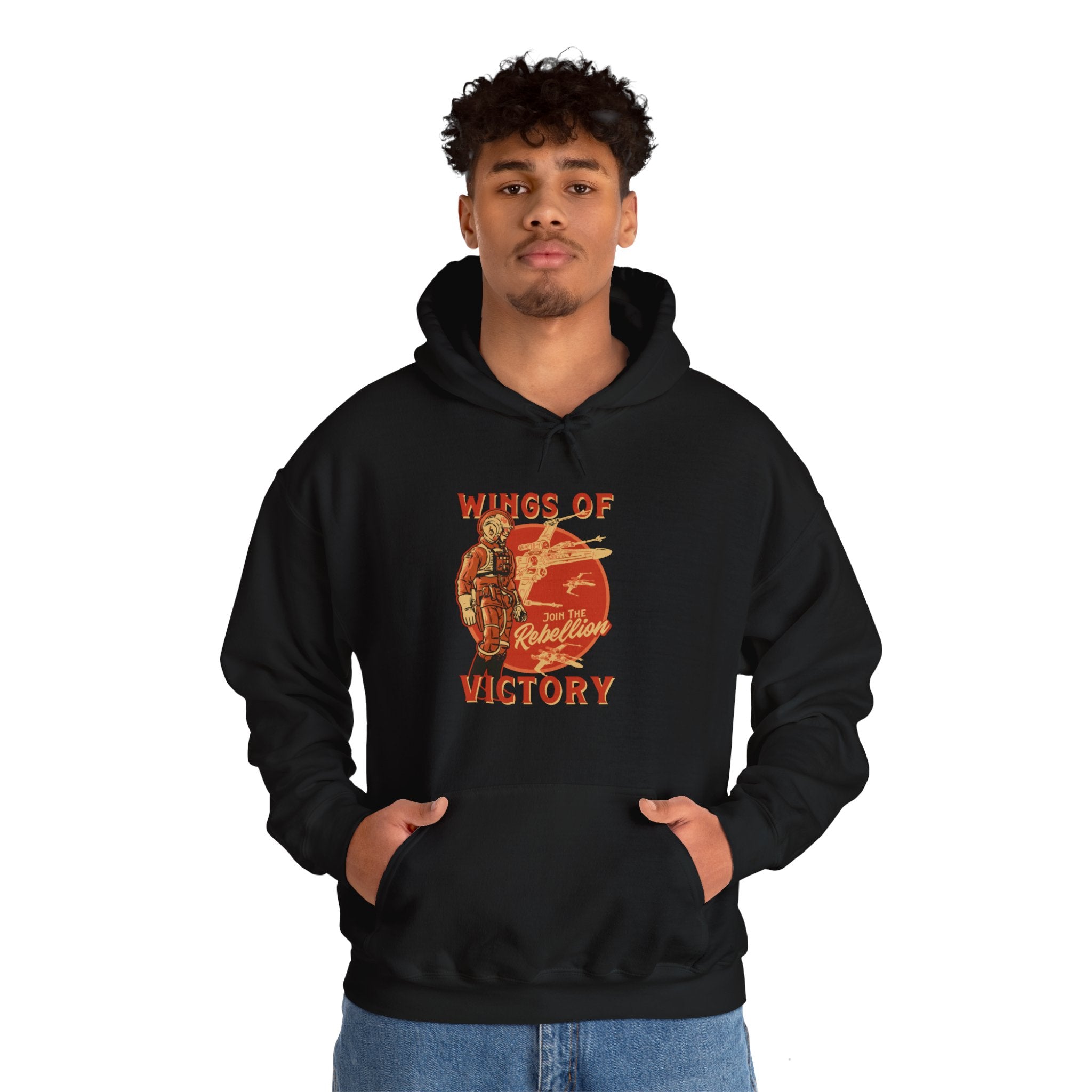 A person stands with hands in pockets, wearing a black Wings of Victory - Hooded Sweatshirt featuring a vintage aircraft graphic on the front, capturing a perfect blend of fashion and nostalgia.