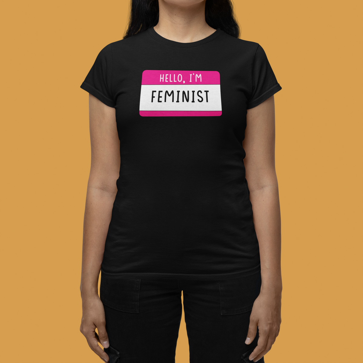 Hello I'm Feminist name tag T-shirt in black, woman wearing it against an orange backdrop, gift tee