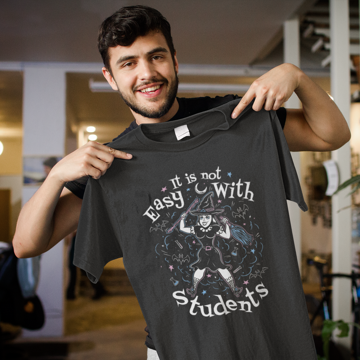 'It Is Not Easy With Students' t-shirt in black, smiling man holding it up, funny teacher gift shirt