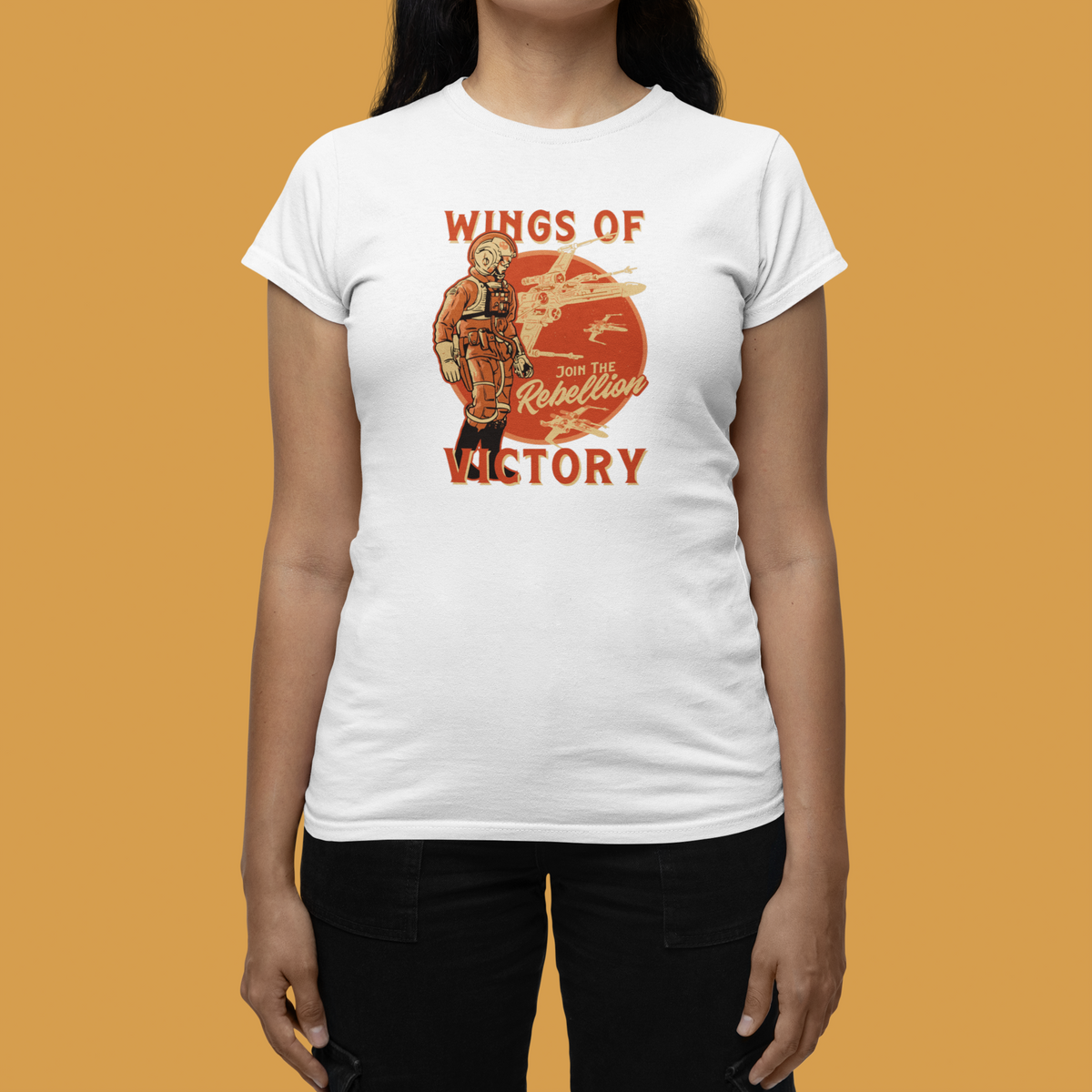 'Wings of Victory' women's tee in white, flat lay front on mustard background, warrior graphic tee