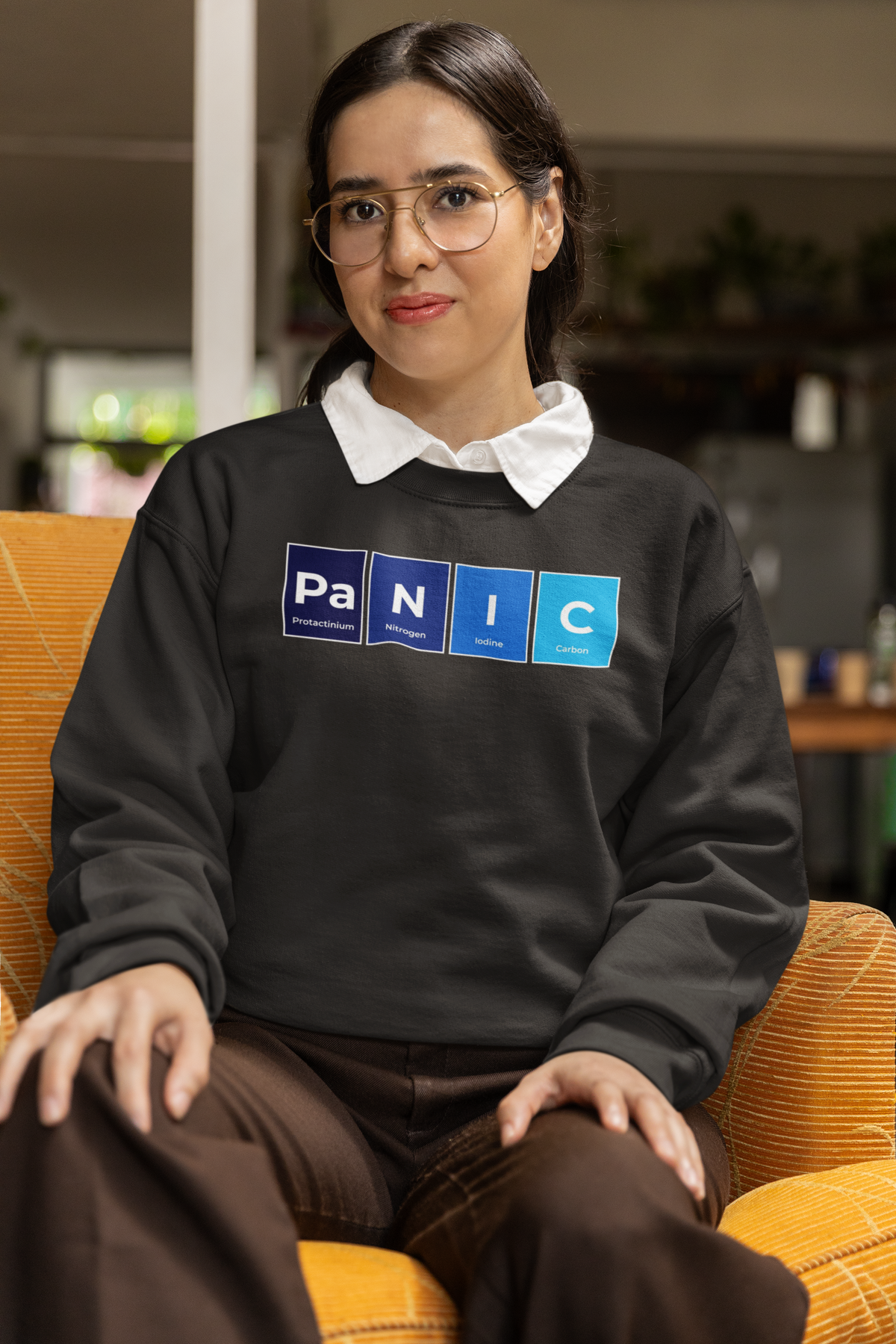 'Pa-N-I-C' periodic table sweatshirt in black, woman sitting on a couch wearing it, cozy lifestyle photo