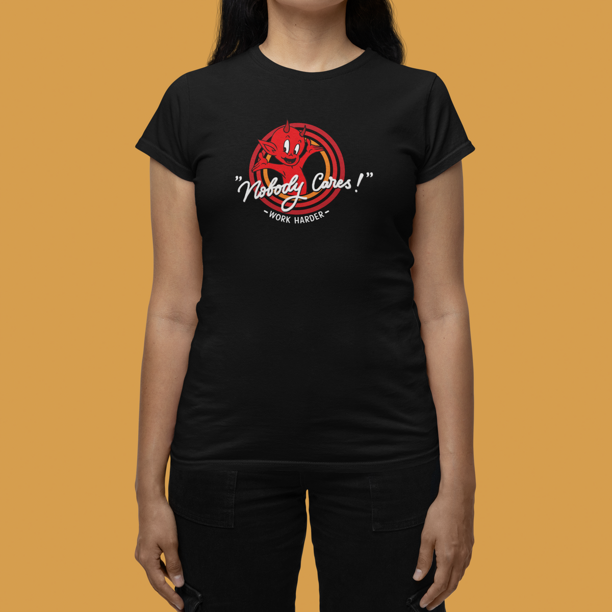 "Nobody Cares, Work Harder" devil graphic tee in black, woman wearing it on tan backdrop, motivational gift for her