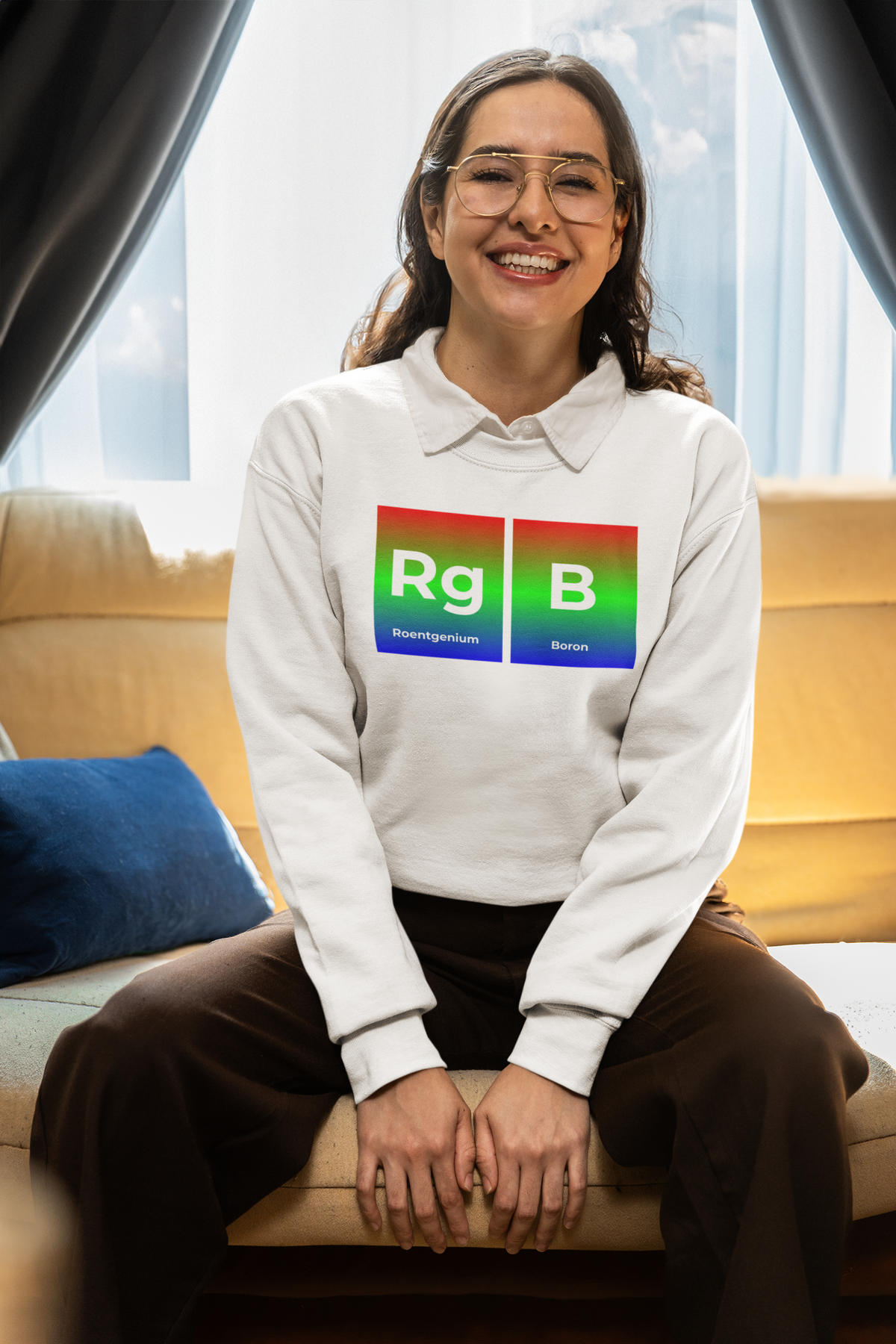 'RG-B' periodic table sweatshirt in white, smiling woman wearing it at home, cozy lifestyle photo