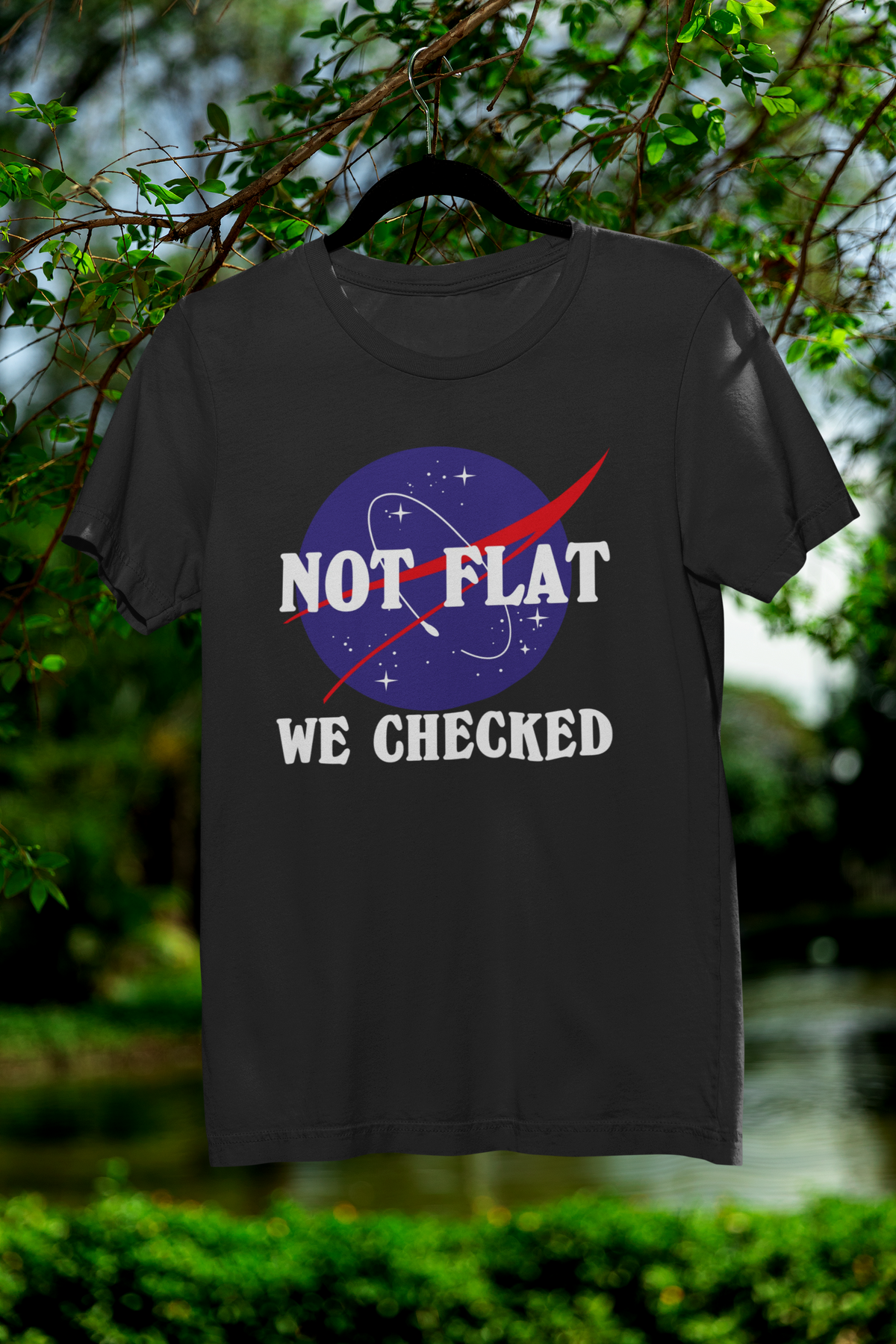 'Not Flat, We Checked' earth logo t-shirt in black, hanging outdoors on a hanger, funny science gift shirt