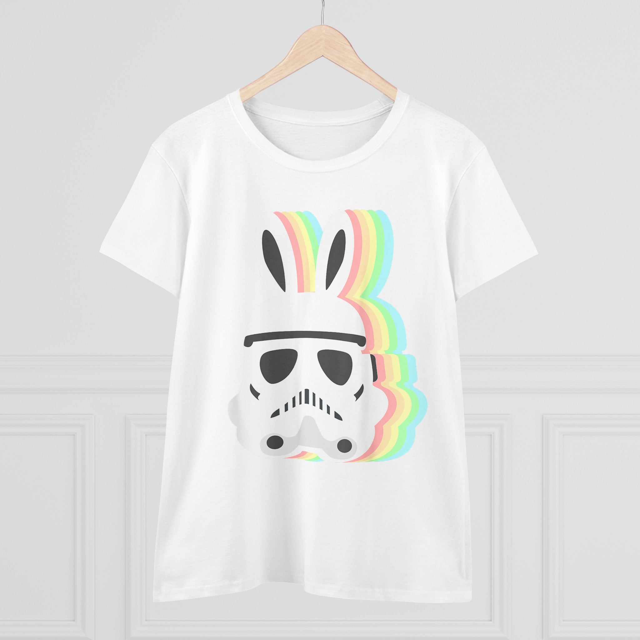 A white Star Wars Easter Stormtrooper - Women's Tee with a design featuring a black stormtrooper helmet adorned with bunny ears, dubbed the Easter Stormtrooper, and overlapping rainbow-colored shadows. The shirt is hung on a wooden hanger against a white wall.