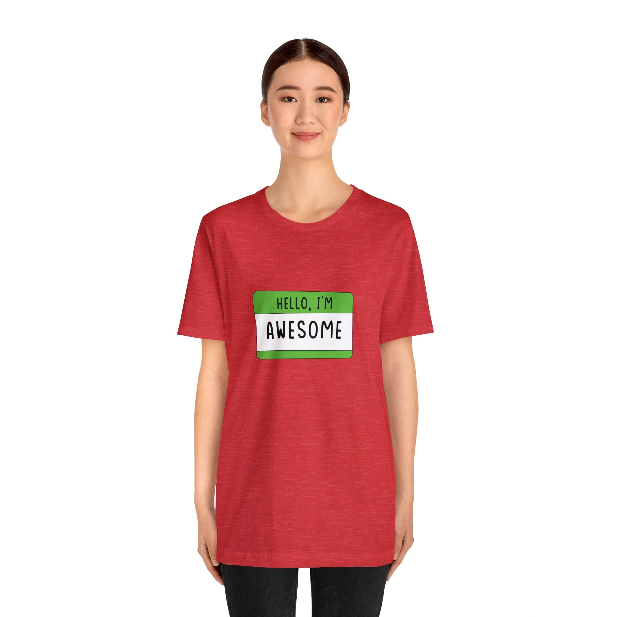 A young woman in a red Hello, I'm Awesome T-shirt with a green "hello, i'm awesome" name tag stands smiling.