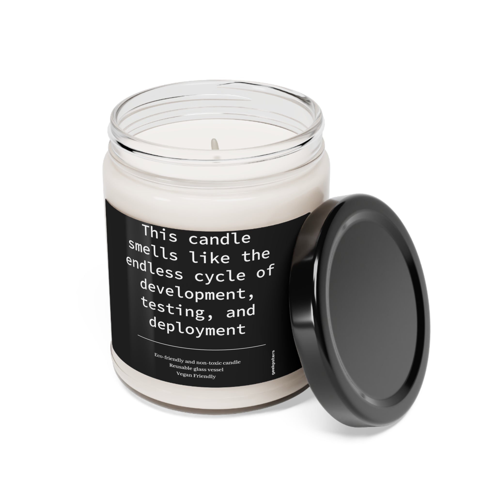 A "This Candle Smells Like the Endless Cycle of Development, Testing and Deployment" scented soy candle in a glass jar with a label stating "this candle smells like the endless cycle of development, testing, and deployment," alongside an open black lid.