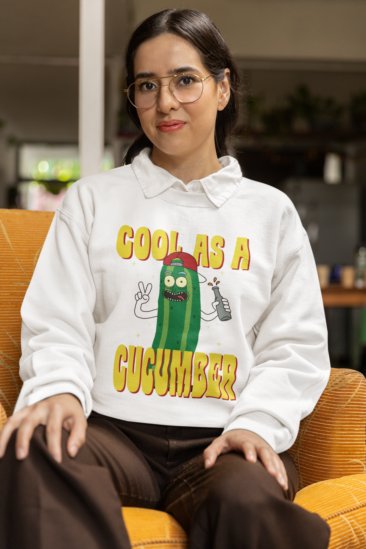 "Cool As A Cucumber" cartoon graphic sweatshirt in black, woman wearing it seated in glasses, funny pun gift