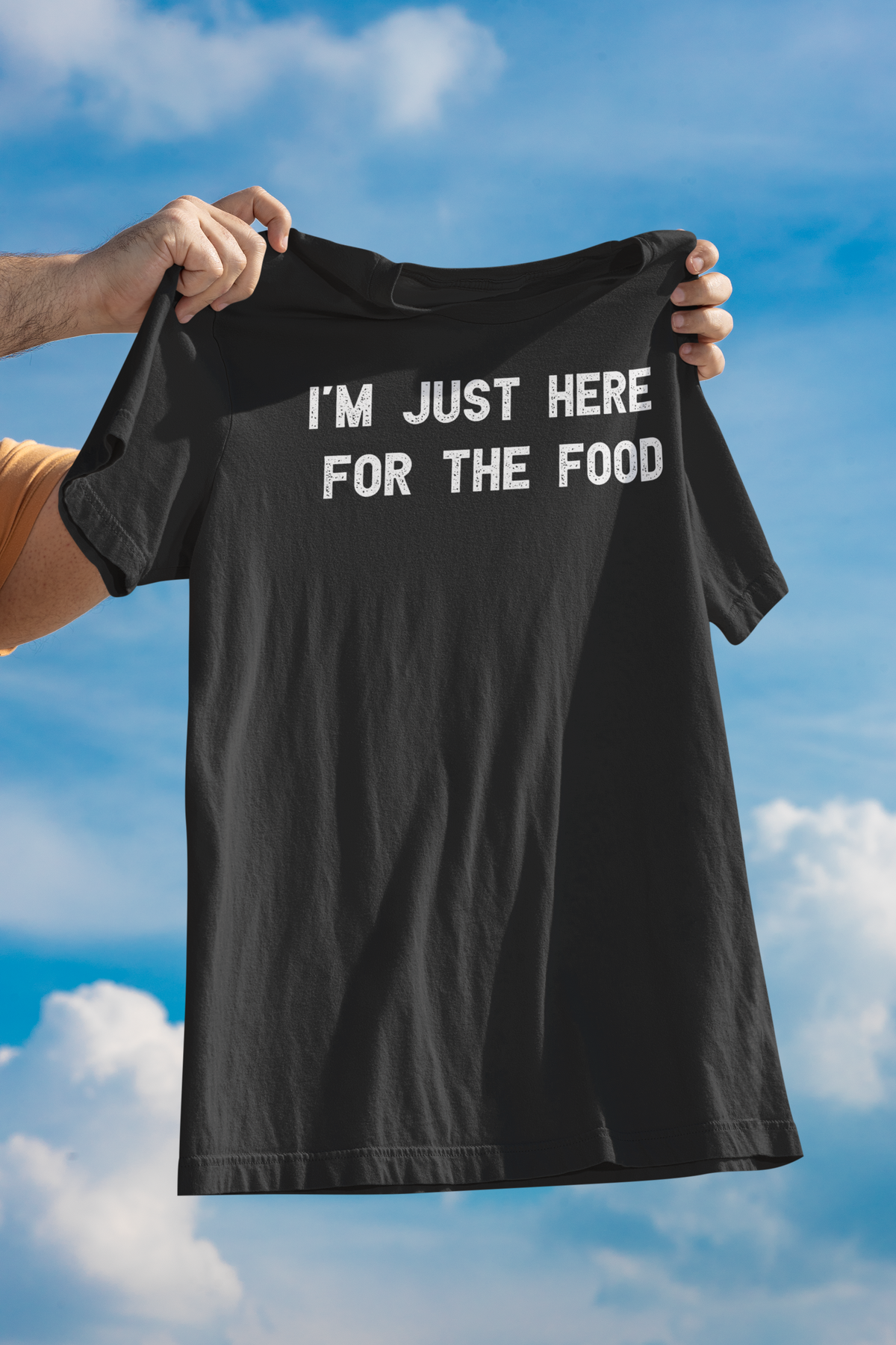 'I'm Just Here for the Food' t-shirt in black, person holding it up against a blue sky, funny foodie graphic tee gift