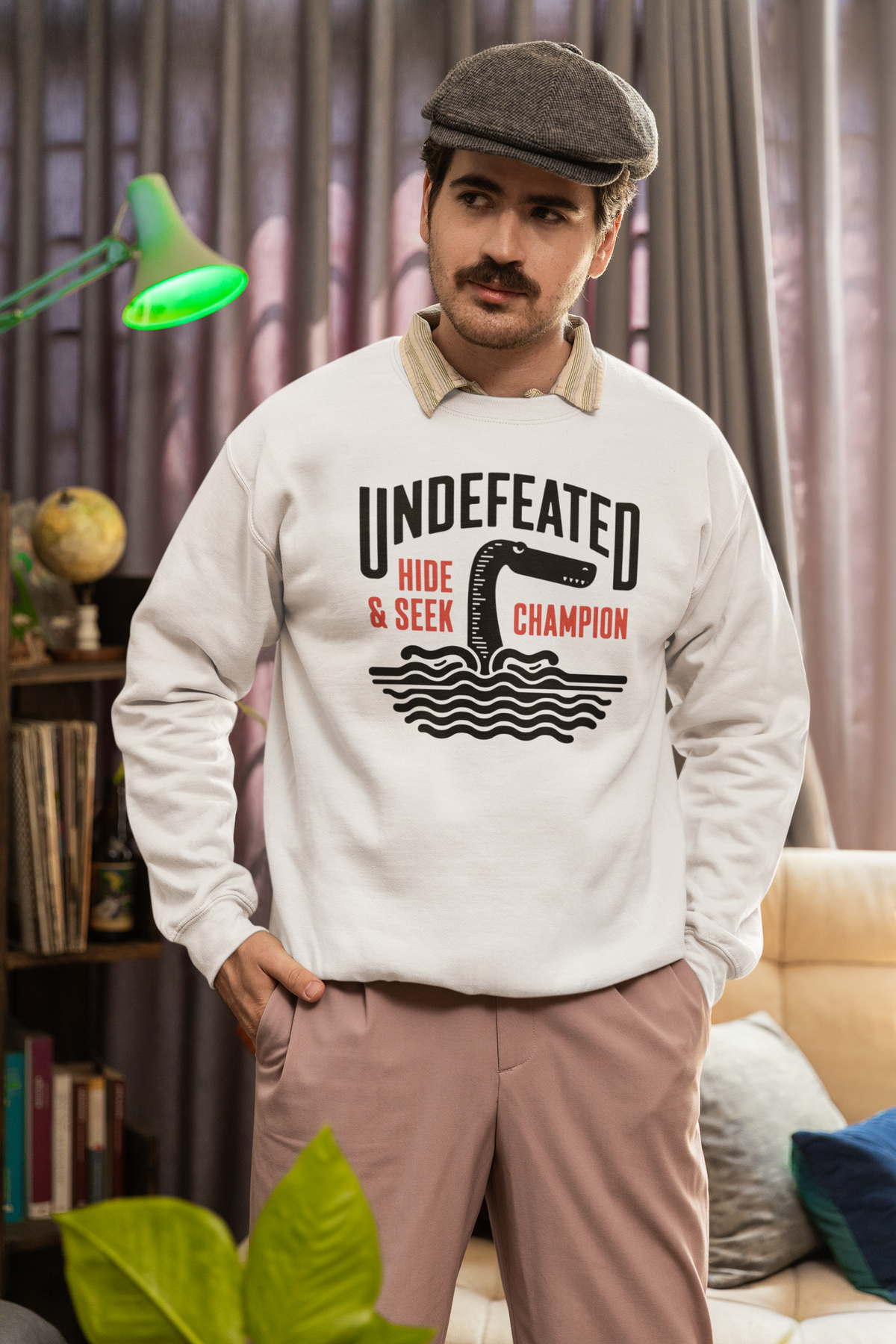 "Undefeated Hide and Seek Champion" sweatshirt in cream, man wearing it indoors, funny gift for gamers