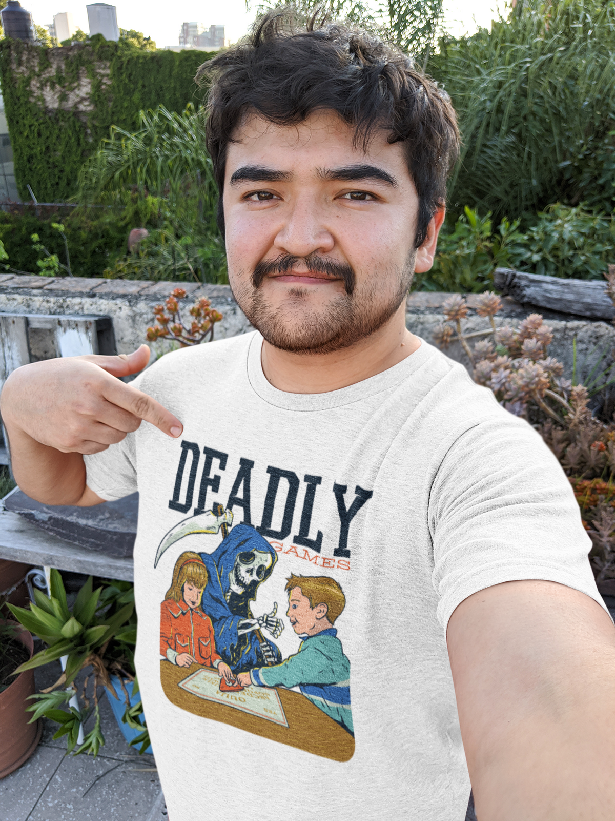 'Deadly Games' t-shirt in white, man model wearing it outdoors among rocks and greenery, funny gift for gamers