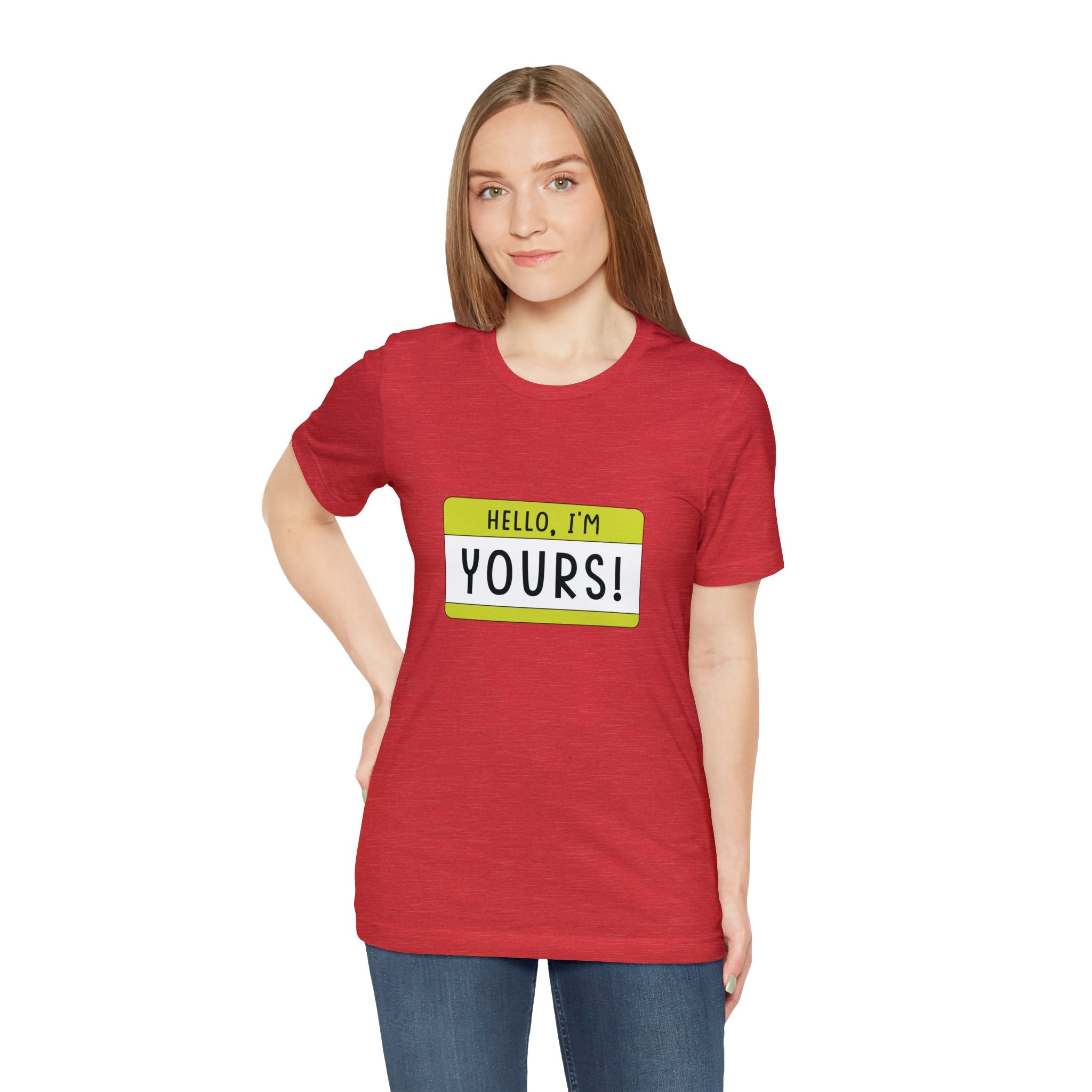 A woman in a red "Hello, I'm YOURS" t-shirt with a geeky demeanor stands facing the camera.
