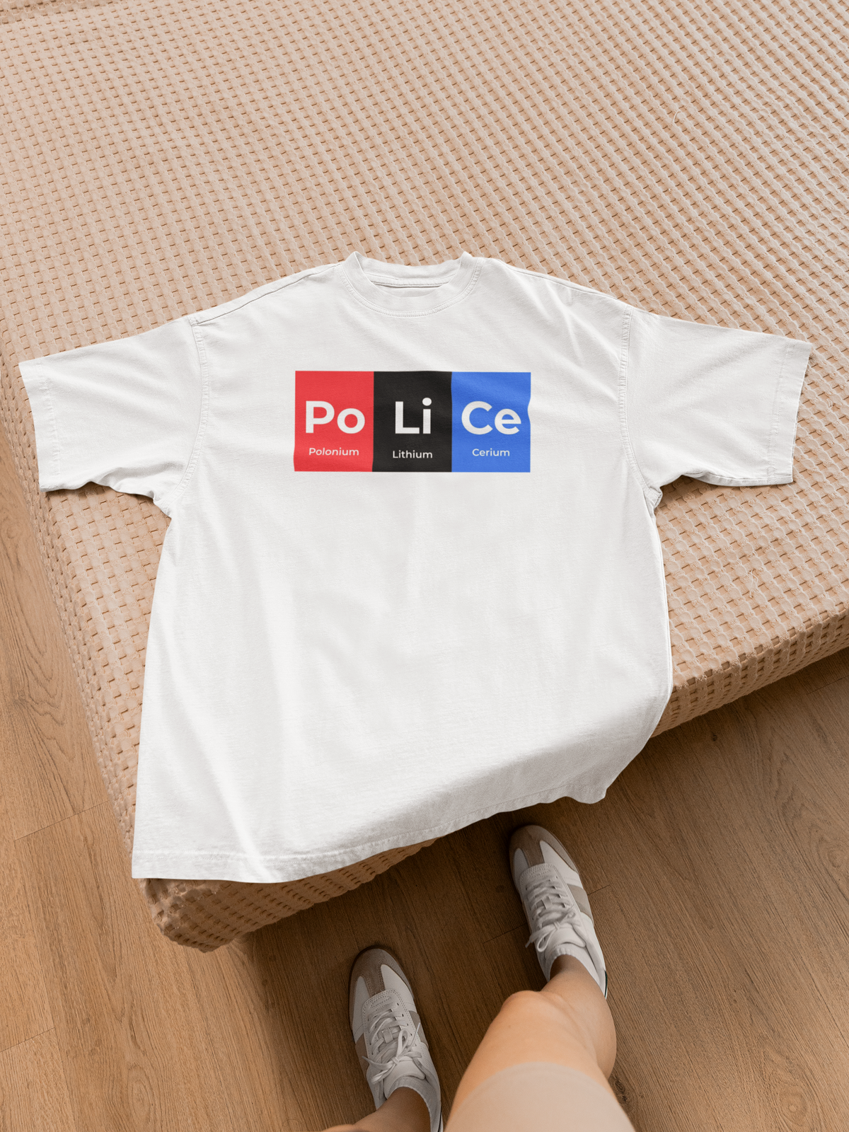 'Po-Li-Ce' periodic table t-shirt in white, flat lay on a bed with sneakers, casual lifestyle photo