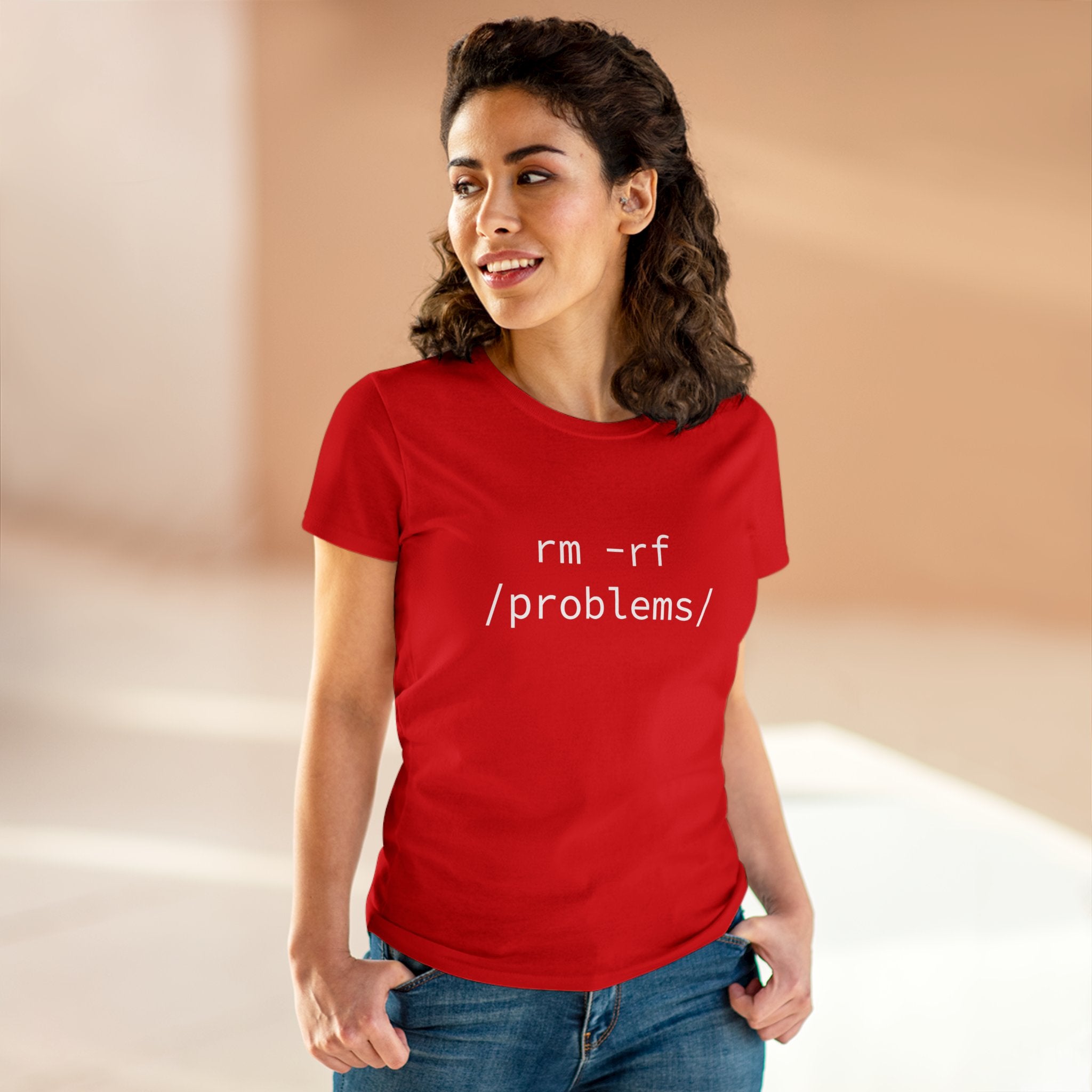 In a softly lit room, an individual stands wearing the Women's Tee from RMRF Problems, made from pre-shrunk cotton. The red t-shirt features a striking "rm -rf /problems/" design across the front.