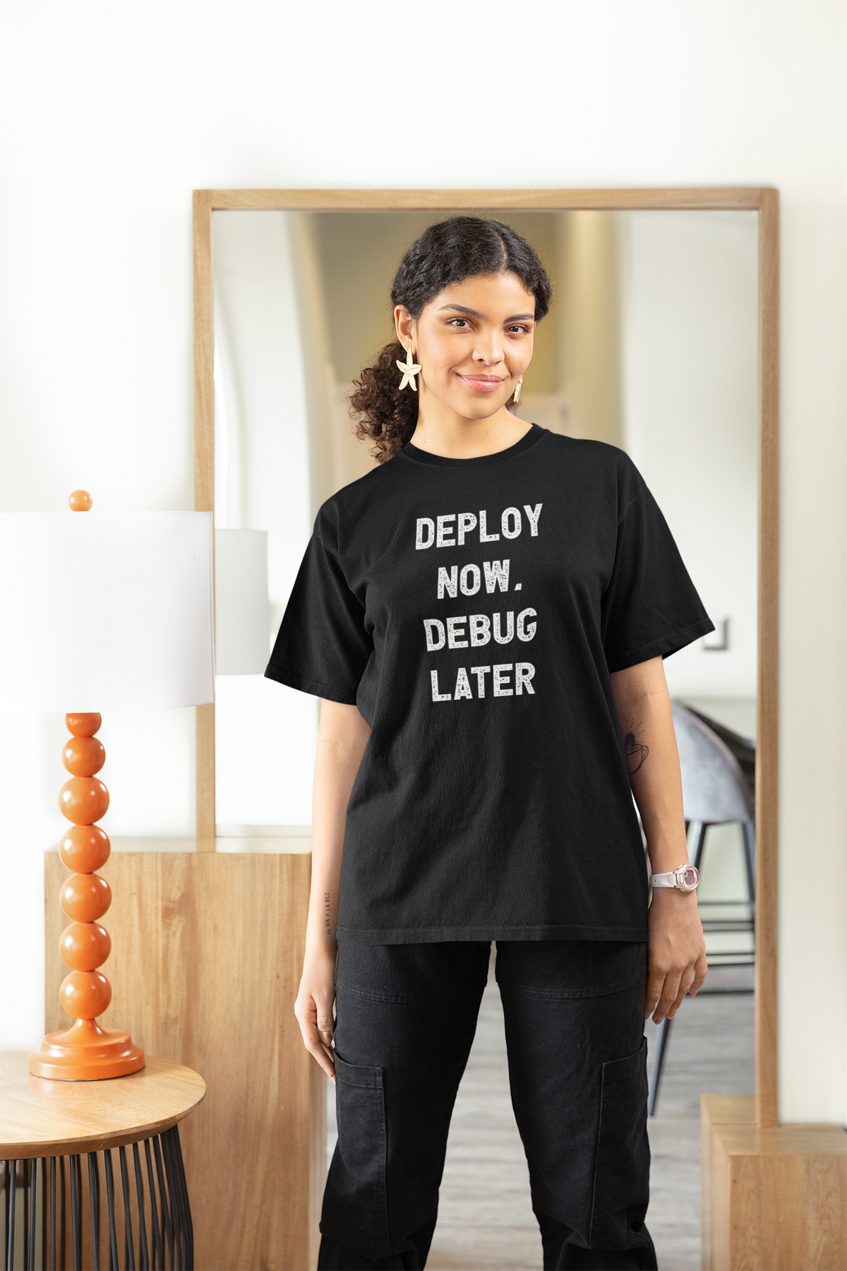 'Deploy Now, Debug Later' t-shirt in black, woman wearing it at home, funny gift for female programmers