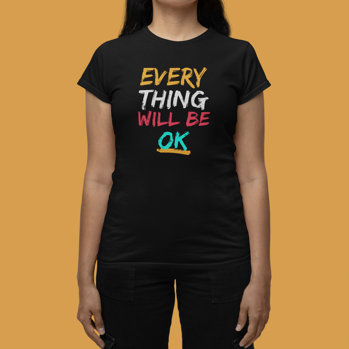'Everything Will Be OK' Women's T-Shirt in black, woman modeling it against an orange backdrop
