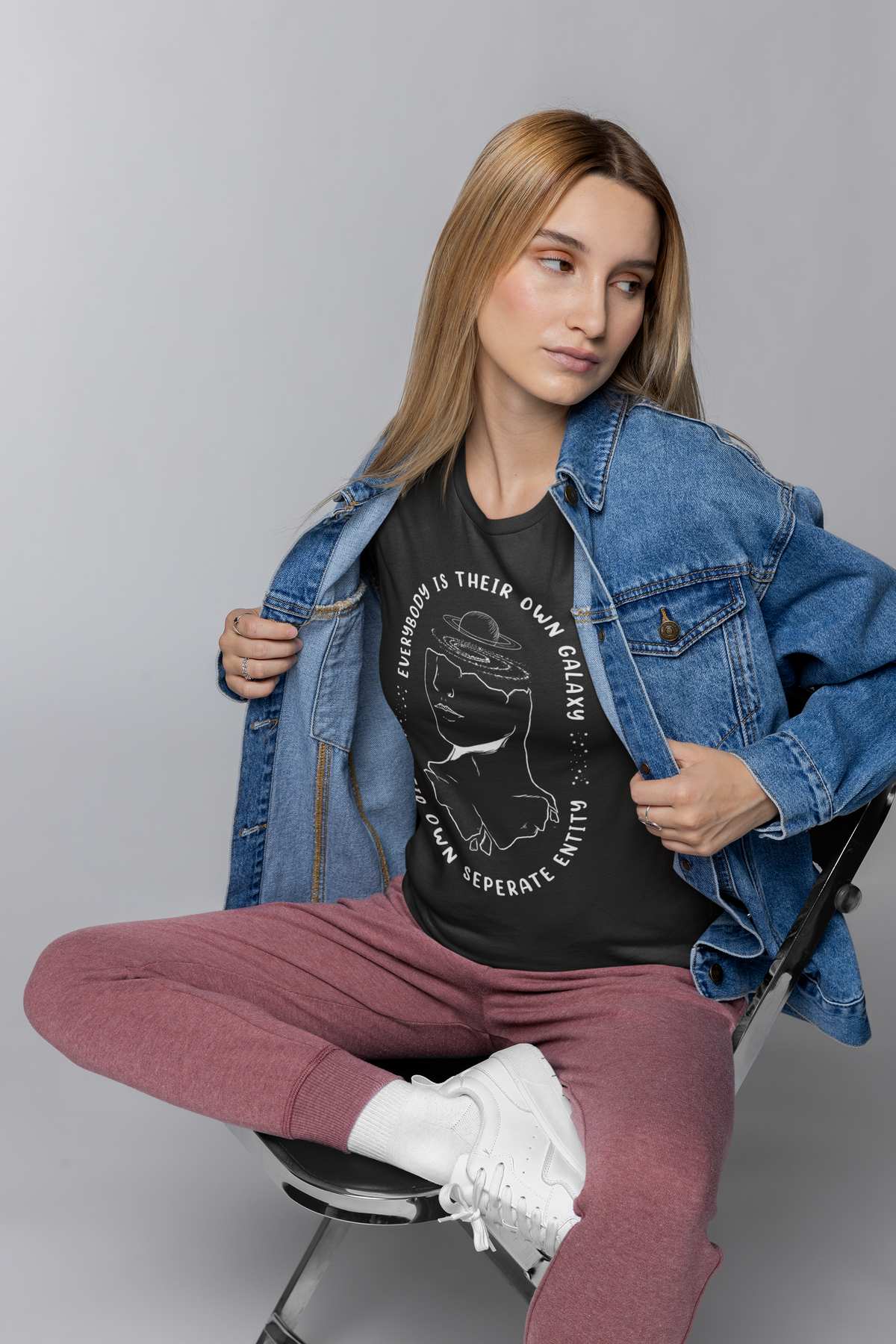 "Everybody Is Their Own Galaxy" graphic t-shirt in black, woman wearing it with denim jacket, quirky astronomy gift