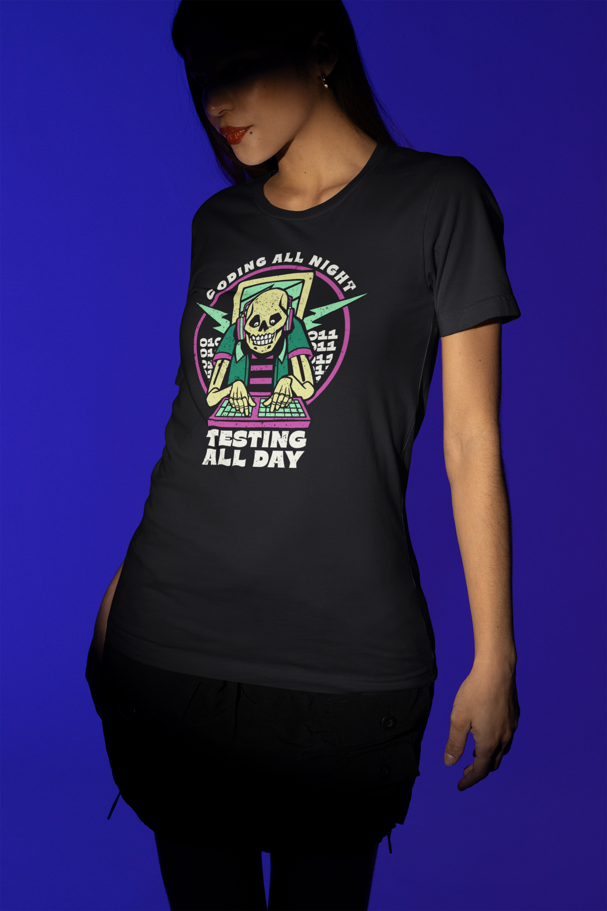 'Coding All Night, Testing All Day' skeleton t-shirt in black, woman model wearing it against a blue background, coder gift