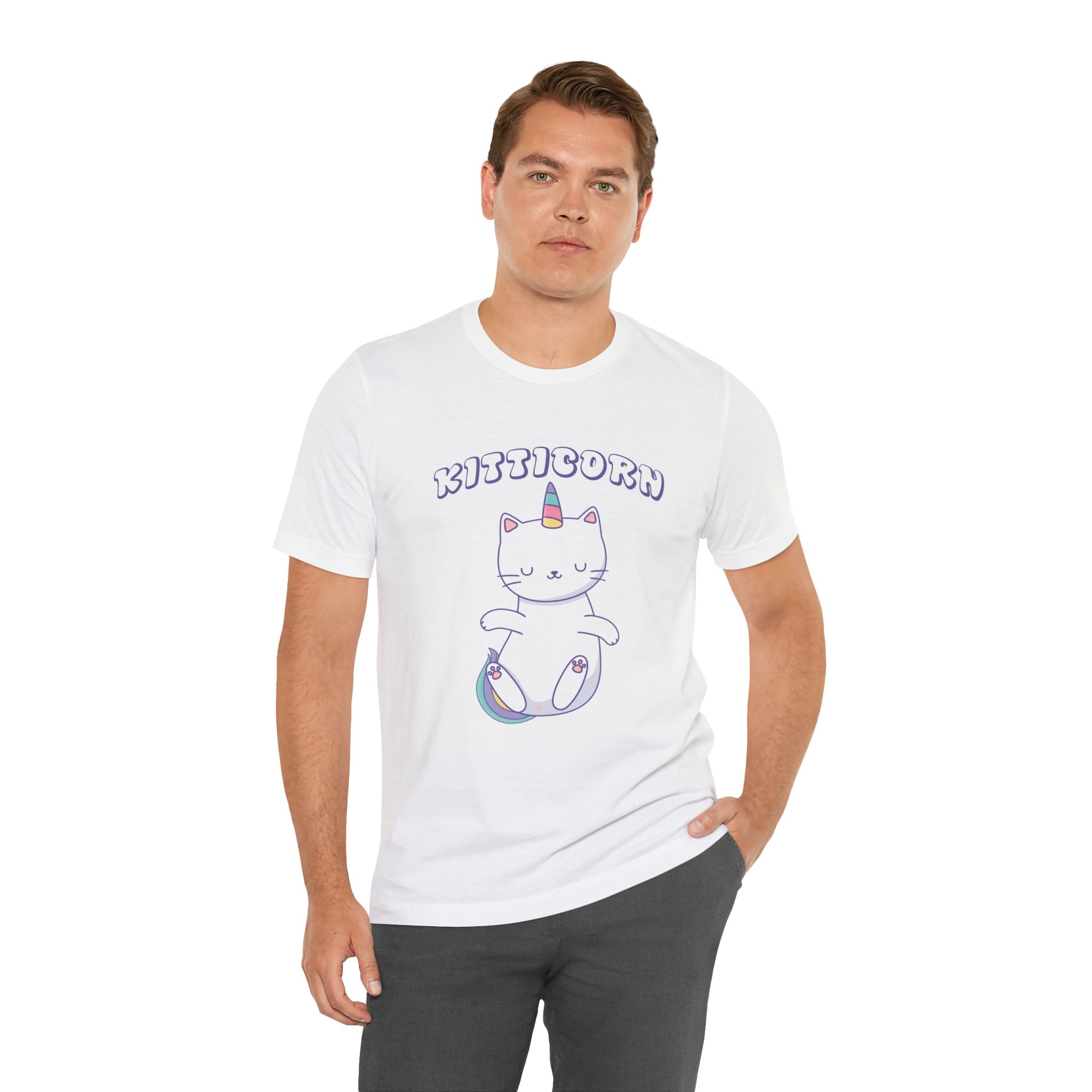 Sentence with product name: Man standing, wearing a white unisex jersey tee with a "Kitticorn" graphic of a cat with a unicorn horn, against a plain background.