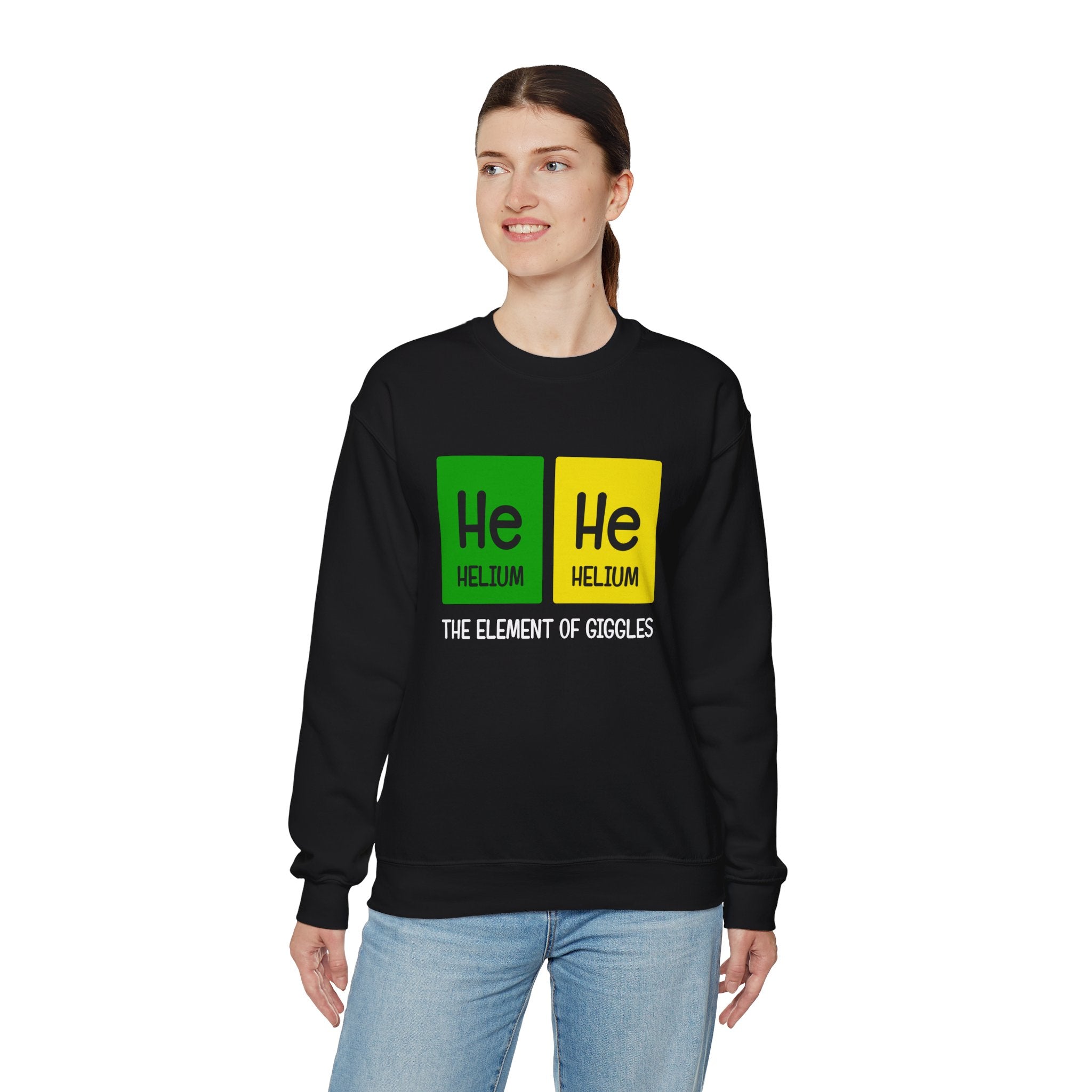 A person in jeans wears a stylish black He-He - Sweatshirt featuring a periodic table design with “He” highlighted in green and yellow, and text below reading “The Element of Giggles.” The coziness of the sweatshirt adds an extra layer of charm to the outfit.