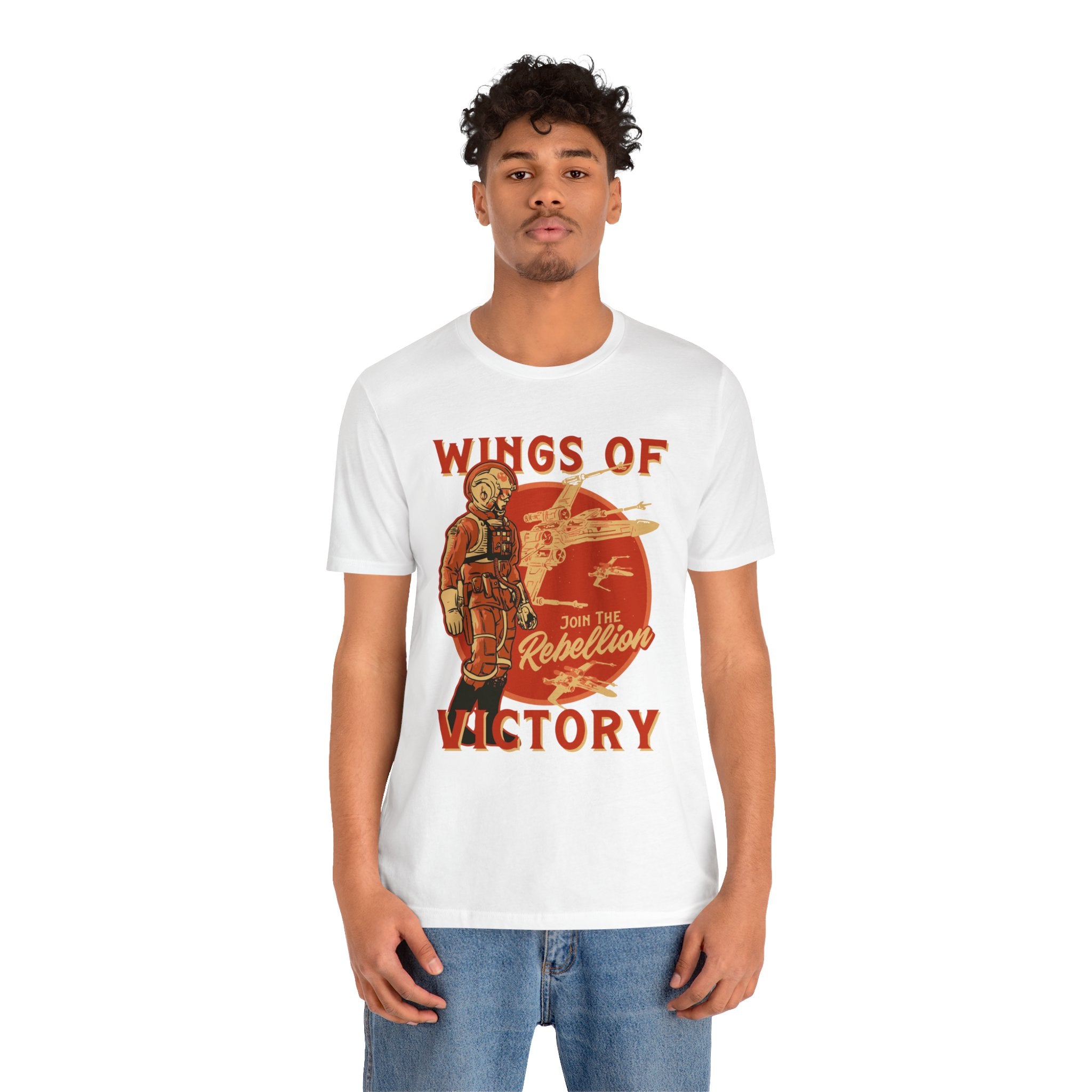 A person is wearing the "Wings of Victory" T-Shirt, a classic unisex jersey tee made from soft cotton. It features the text "WINGS OF VICTORY" along with an illustration of a pilot and aircraft, and has "Join the Rebellion" printed in bold red and orange. The high-quality print guarantees long-lasting wear.