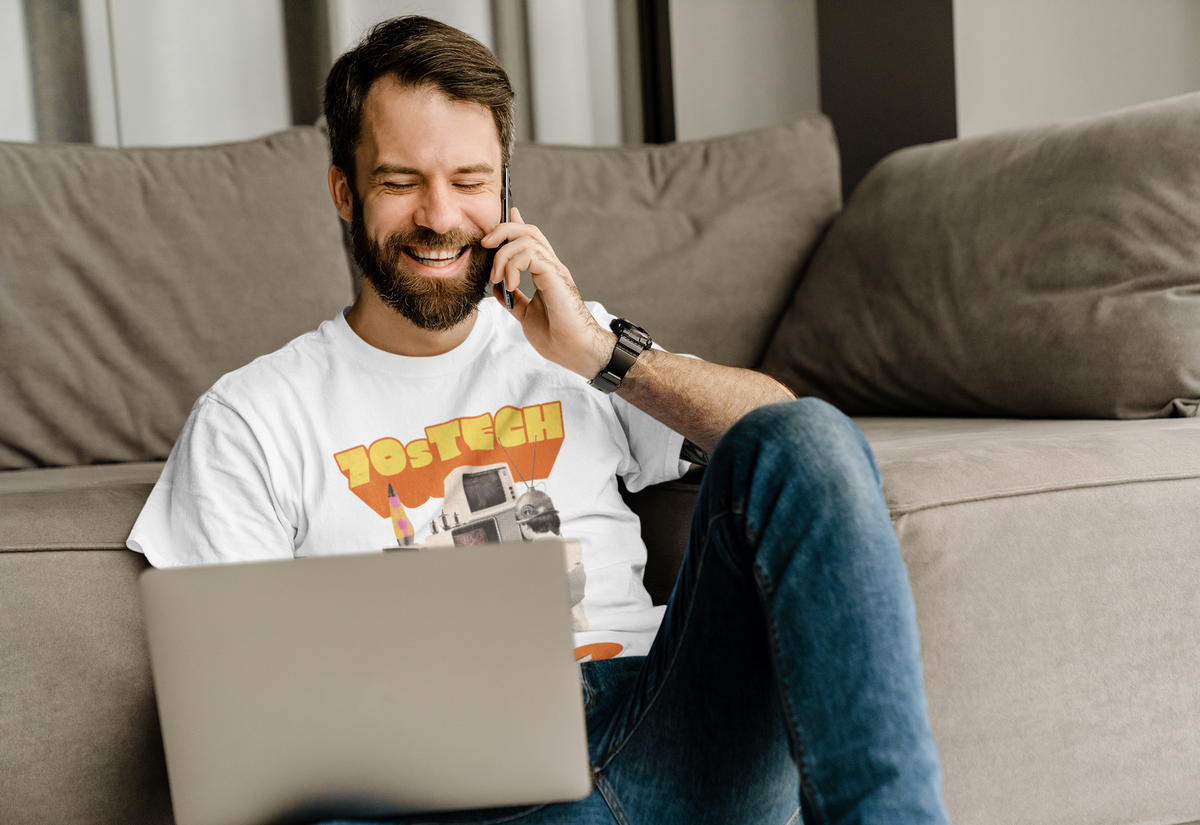 '70s Tech' t-shirt in white, man model wearing it on a couch with a laptop, funny retro geek gift
