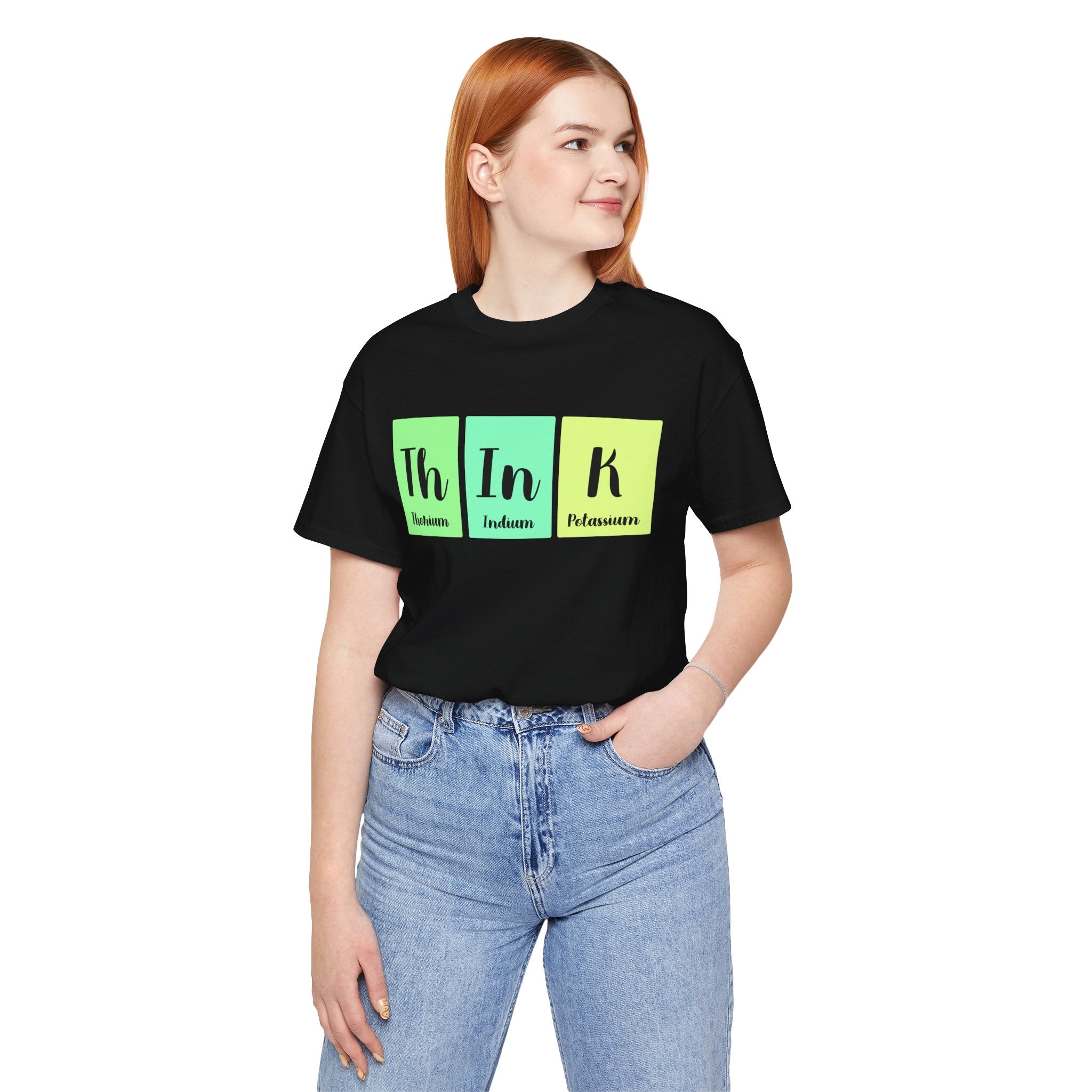 Sentence with Product Name: Woman wearing a black unisex Th-In-k jersey tee with "th in k" printed in green and black, representing chemical elements thorium, indium, and potassium, standing with hands in jeans pockets.