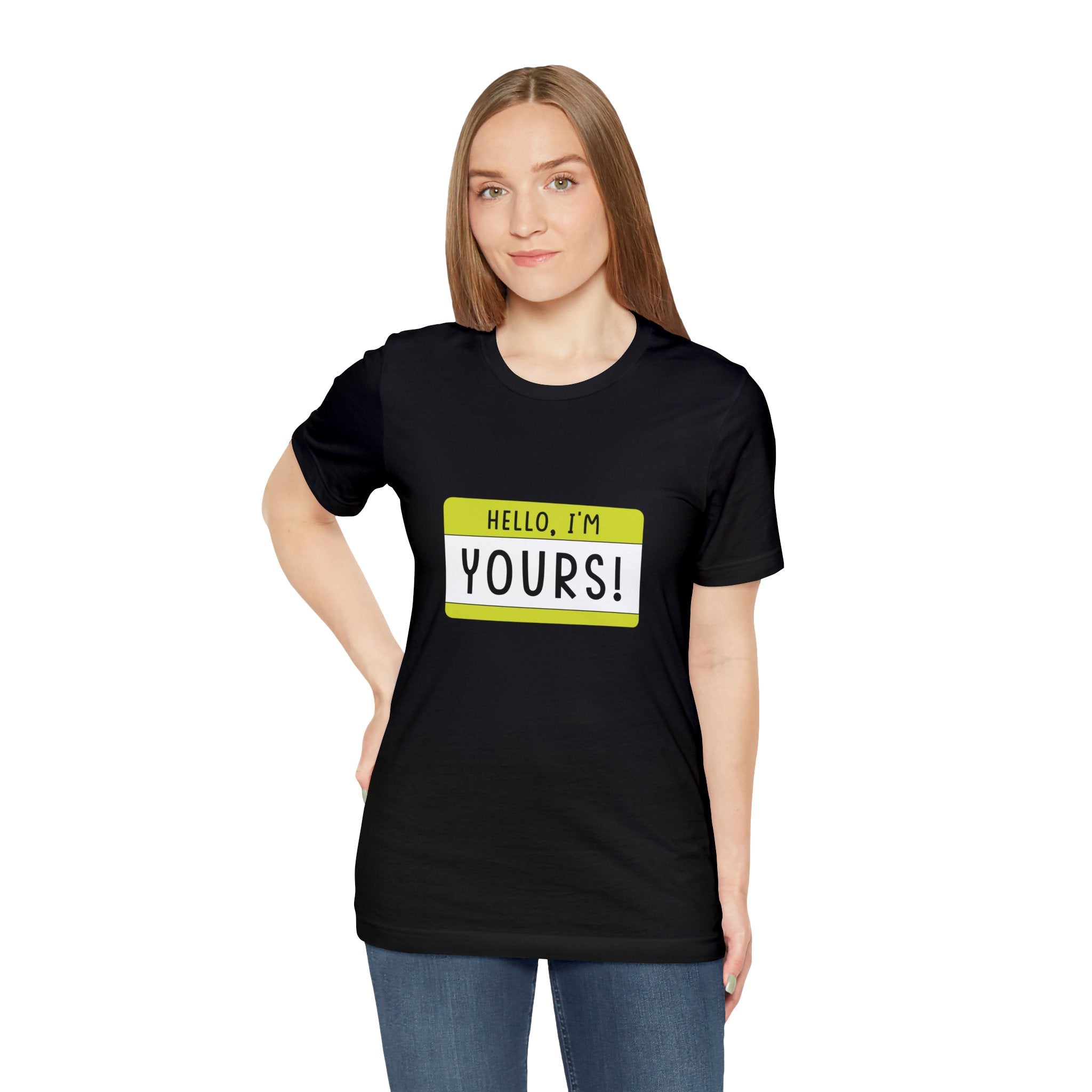 A woman in a black geeky Hello, I'm YOURS T-shirt stands facing the camera.