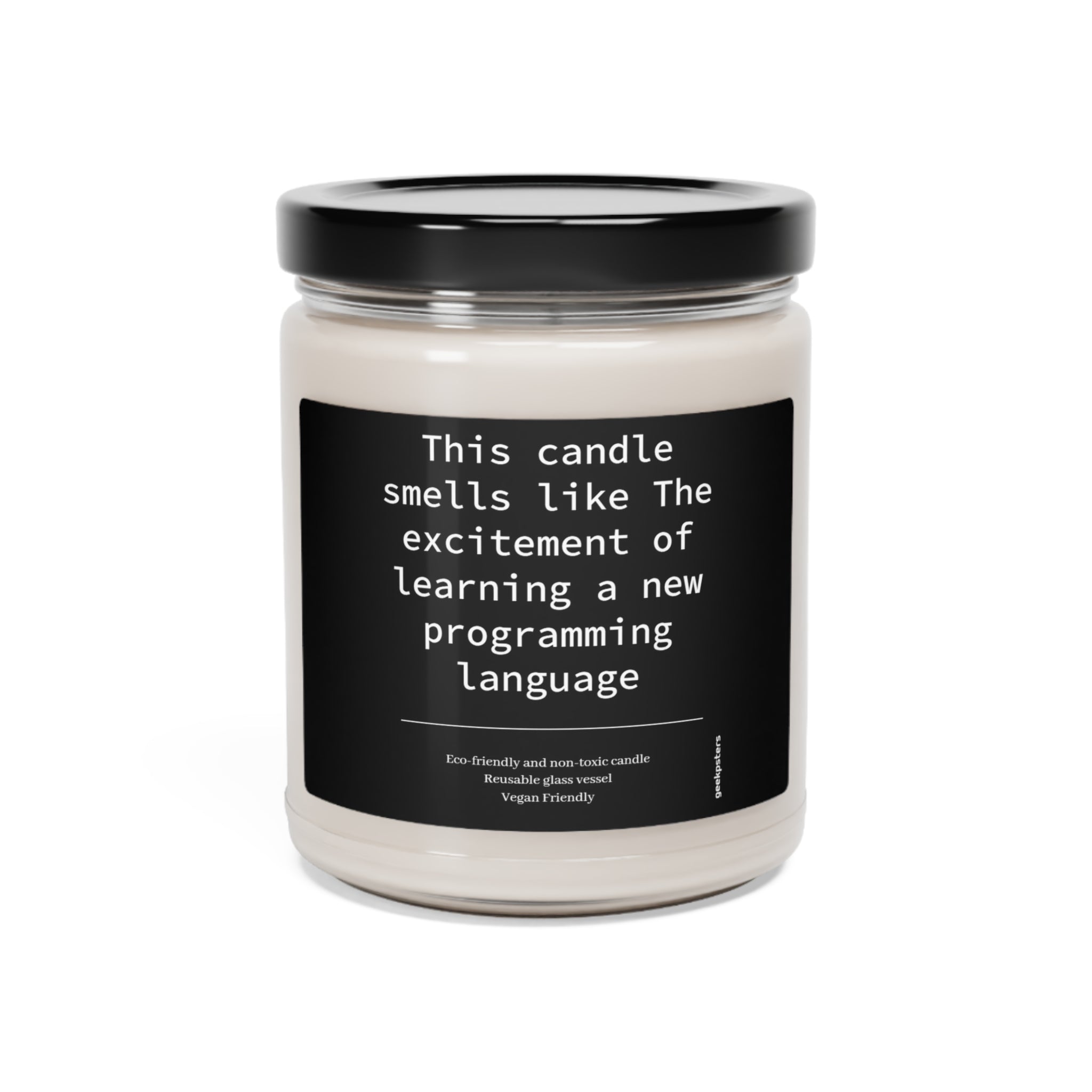 A Scented Soy Candle in a clear jar with a label reading "this candle smells like the excitement of learning a new programming language." Eco-friendly and vegan-friendly text is also visible.