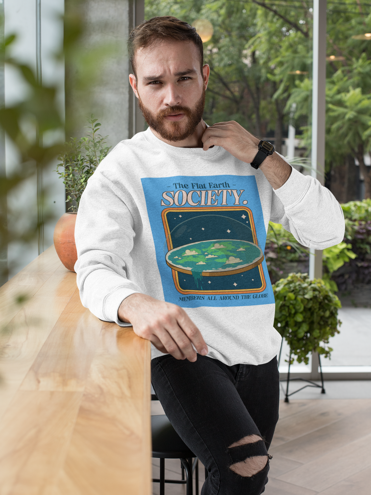 'The Flat Earth Society' sweatshirt in white, bearded man wearing it outdoors, funny satire gift