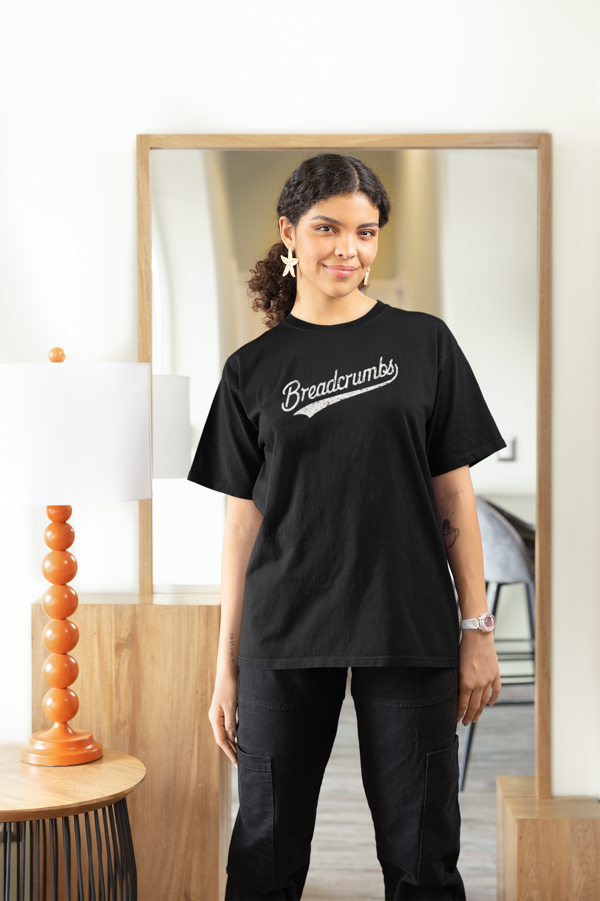 'Breadcrumbs' women's tee in black, woman wearing it in a stylish room, funny retro script logo t-shirt gift