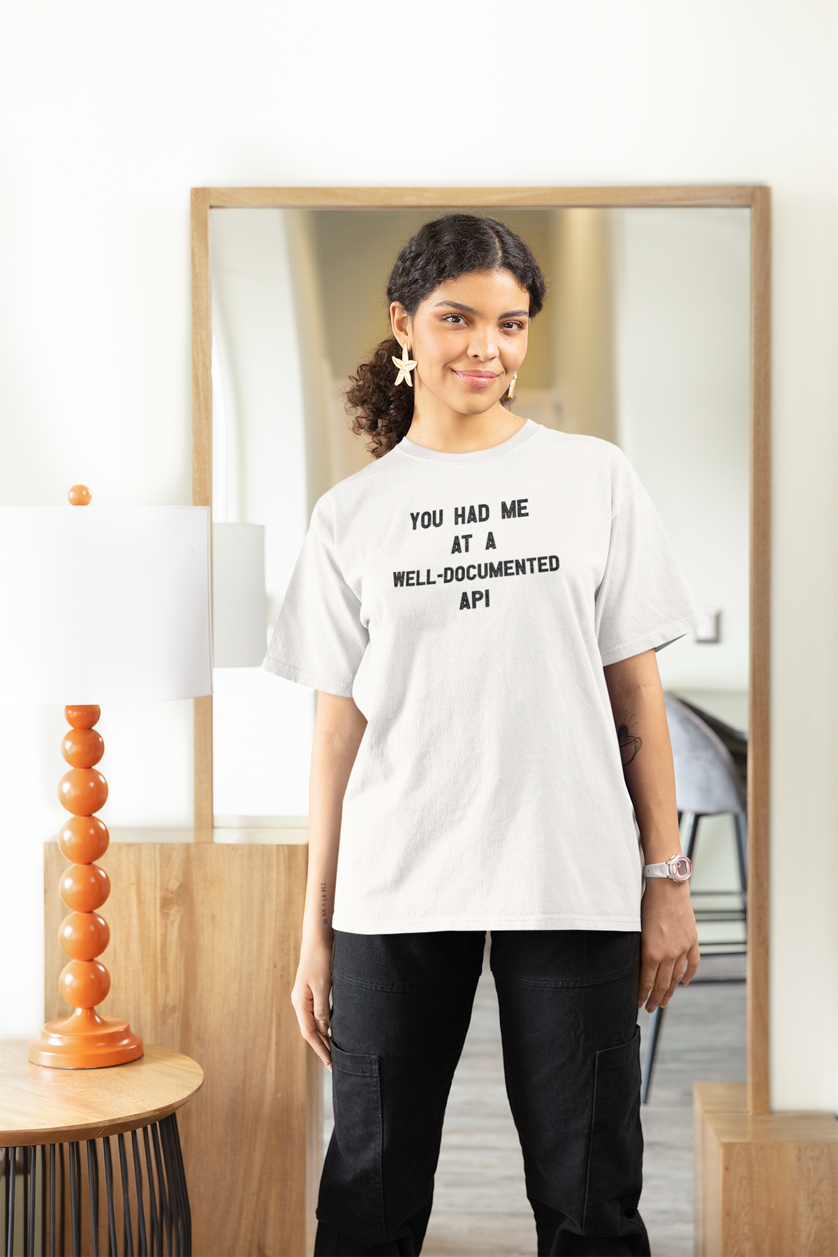 'You Had Me at a Well-Documented API' t-shirt in white, woman wearing it in a stylish room, funny coder pun tee gift